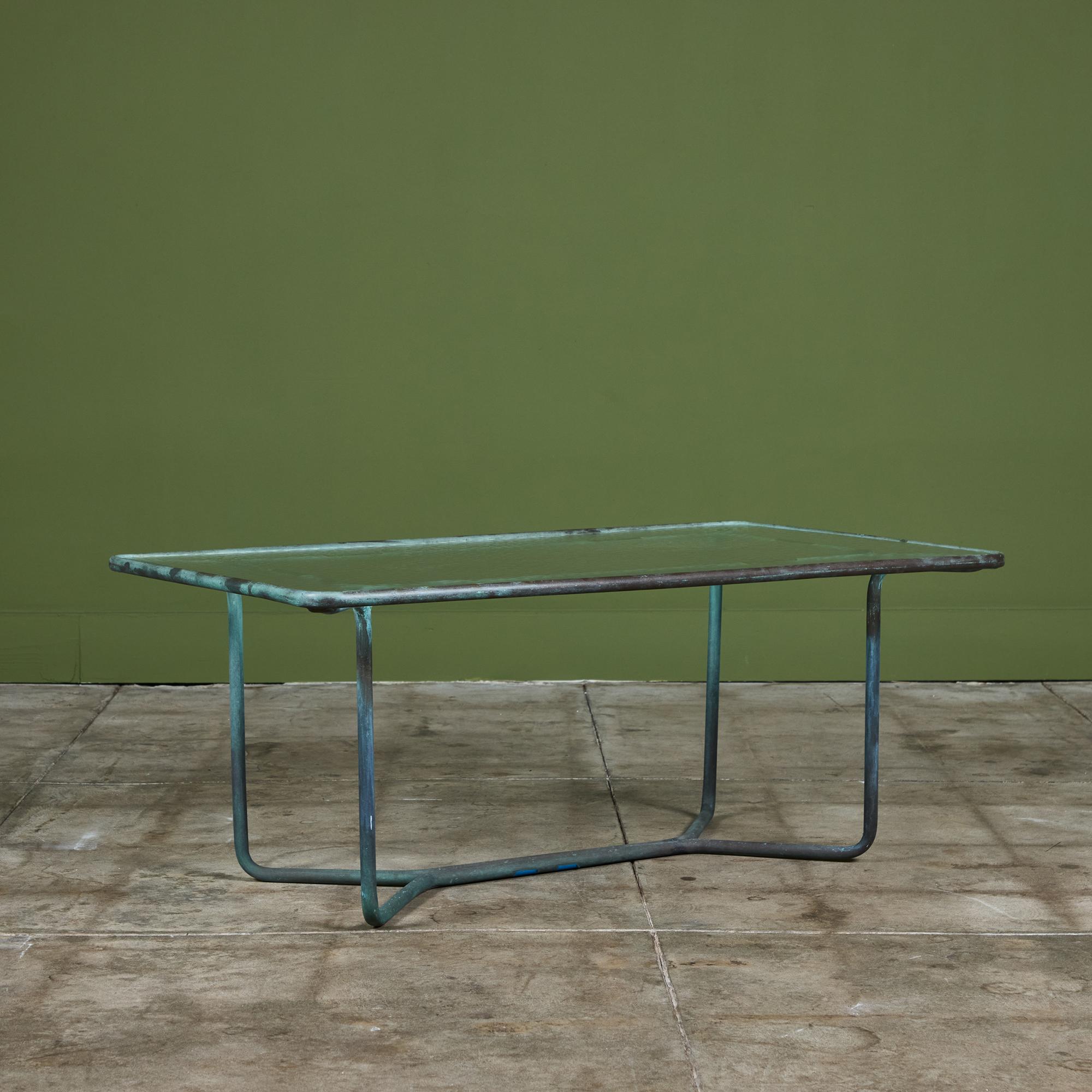 A patio coffee table in patinated bronze designed by Walter Lamb and produced by Brown Jordan. The table has a rectangular shape of tubular patinated bronze with rounded corners, supported by a tubular base in matching bronze. The legs are joined by