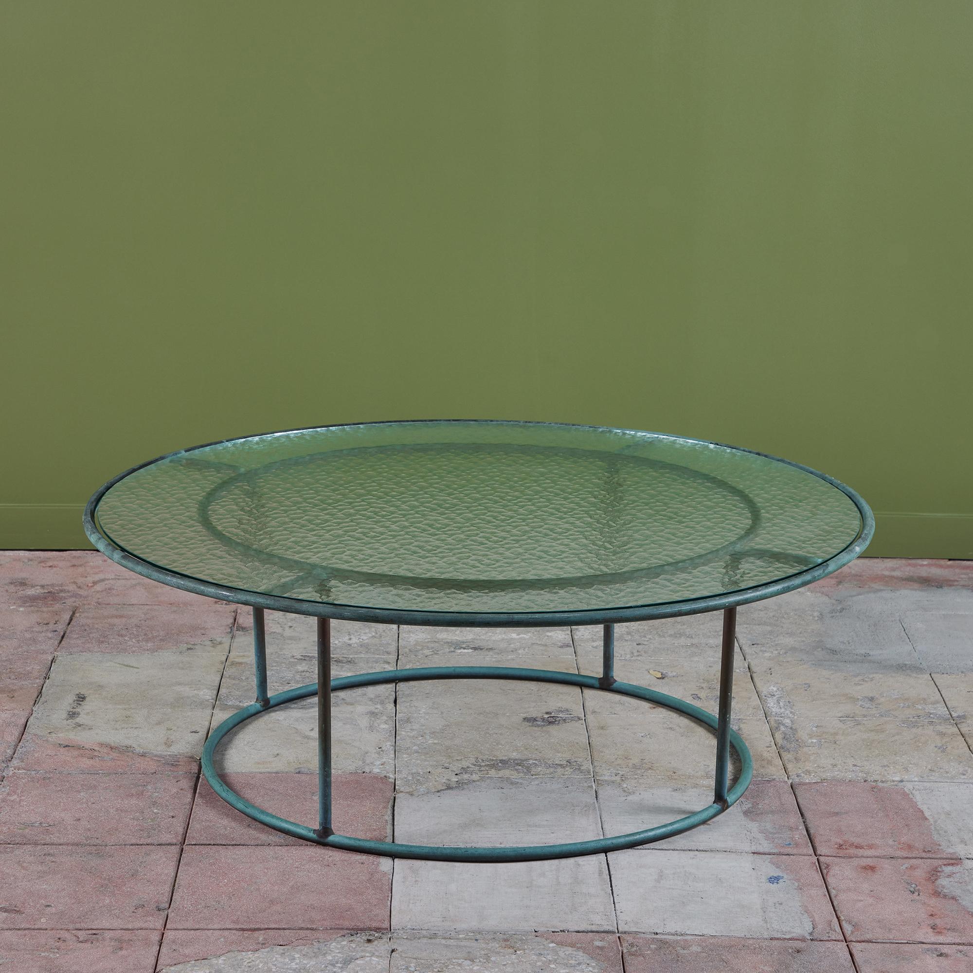Patio coffee table in patinated bronze designed by Walter Lamb and produced by Brown Jordan. The frame is described by two concentric rings of bronze with radial supports and a circular bronze base. The round tabletop is a single piece of hammered