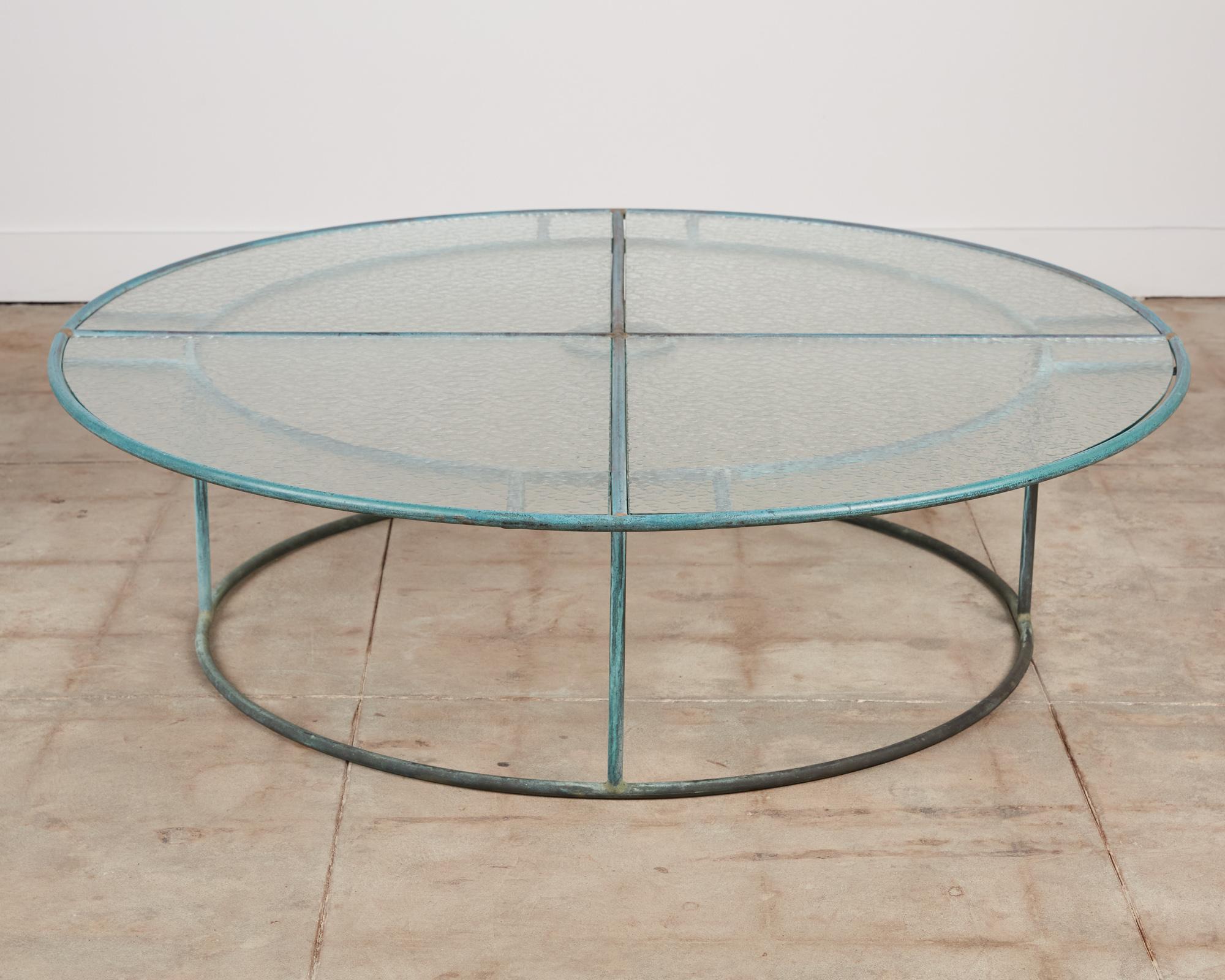 A patio coffee table in patinated bronze designed by Walter Lamb and produced by Brown Jordan. The monumental frame is described by a concentric ring of bronze with radial supports and a circular bronze base.  The round tabletop is made up of 4