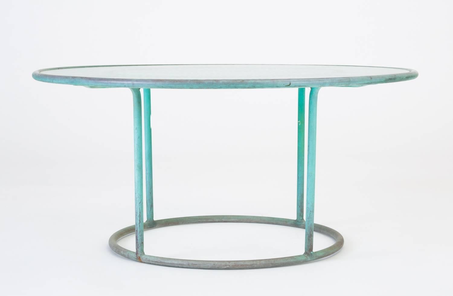 A patio coffee table in patinated bronze designed by Walter Lamb and produced by Brown Jordan. The frame is described by two concentric rings of bronze with radial supports and a circular bronze base. The round tabletop is a single piece of hammered