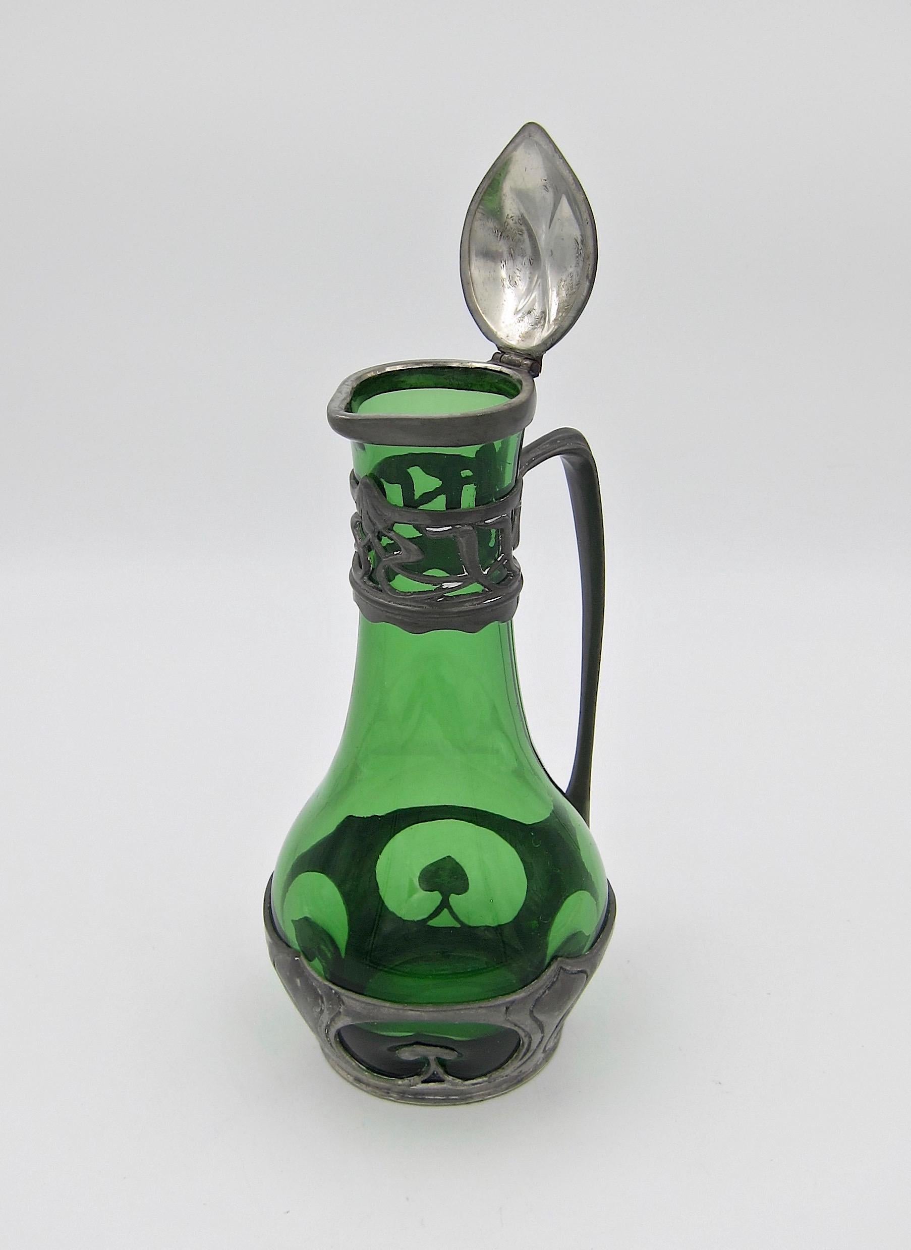 A stylish German green glass carafe with Jugendstil pewter metal mounts. The antique wine carafe was made by Walter Scherf & Company of Nuremberg circa 1900. The ewer / pitcher has a hinged lid with a bud finial and a looped handle joining two
