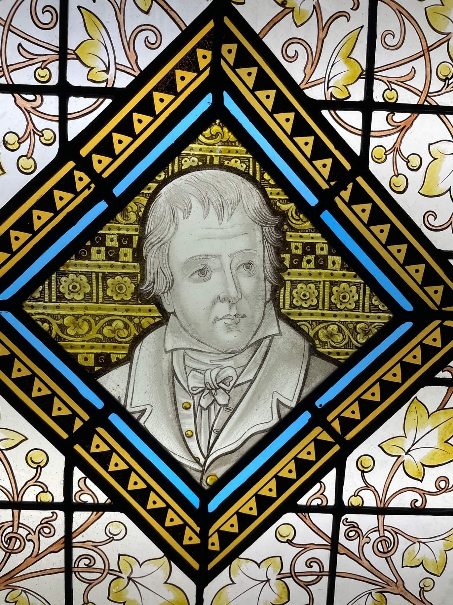 A late 19th century antique stained glass window panel depicting Sir Walter Scott, one of 3 similar we are selling depicting notable figures of British history. At the centre is a distinguishable illustration of Sir Walter Scott, late 18th/early