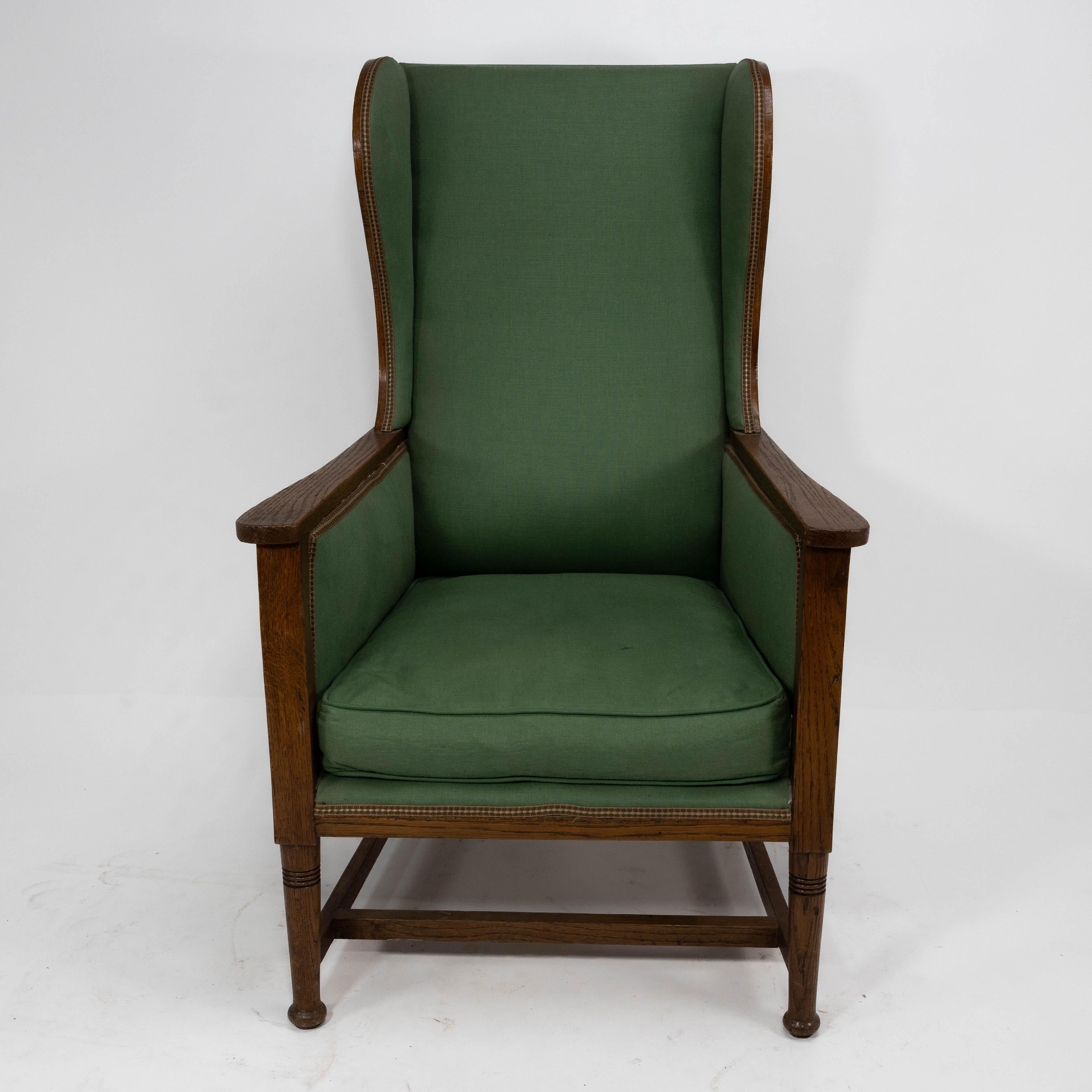 Walter Skull High Wycombe. An Arts and Crafts oak wing back upholstered armchair with lovely show oak to the outer wing sides. The wings curve out and follow down to meet the arms in a free flowing design. The front ring turned legs united with an H