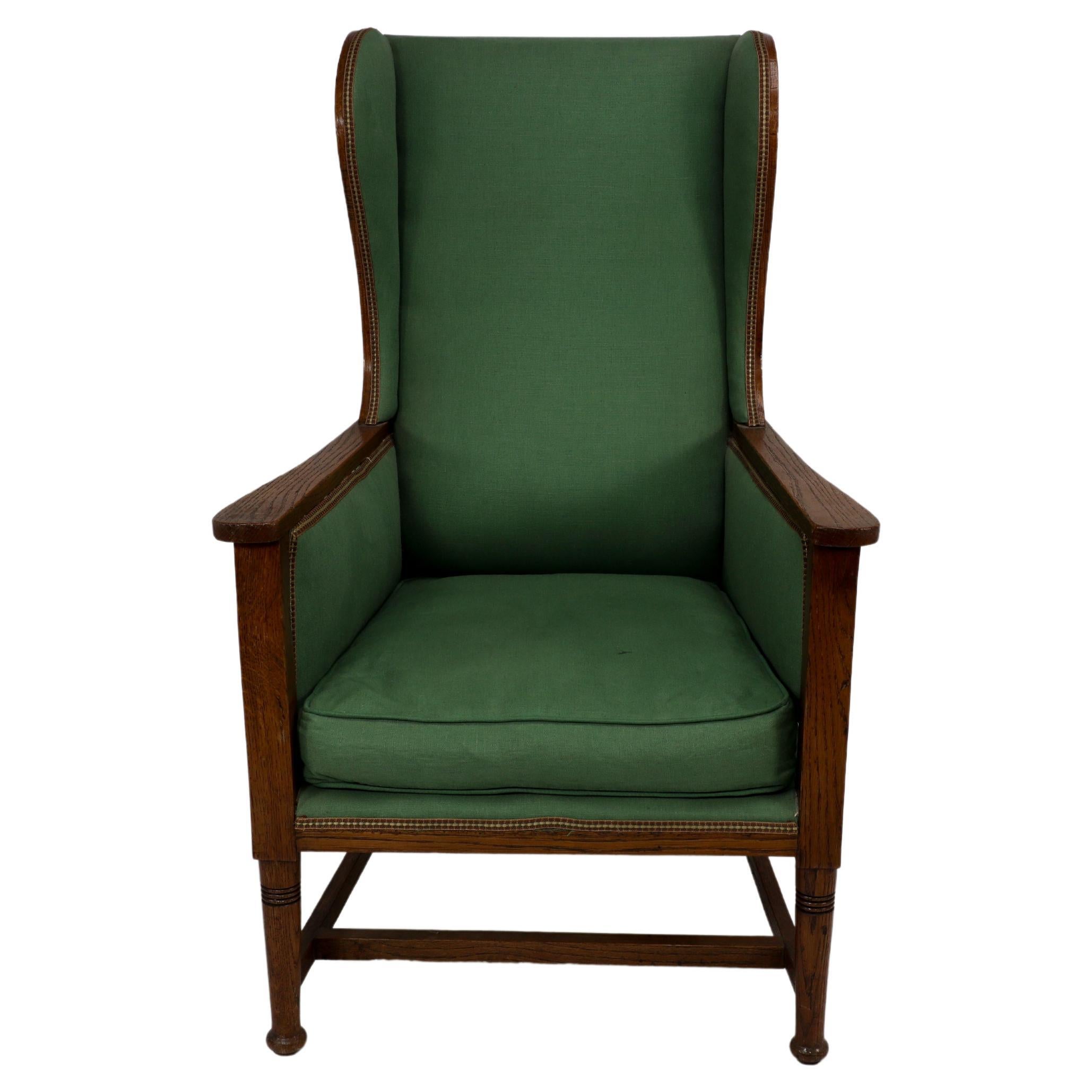 Walter Skull High Wycombe. An Arts and Crafts oak wing back upholstered armchair with lovely show oak to the outer wing sides. The wings curve out and follow down to meet the arms in a free flowing design. The front ring turned legs united with an H