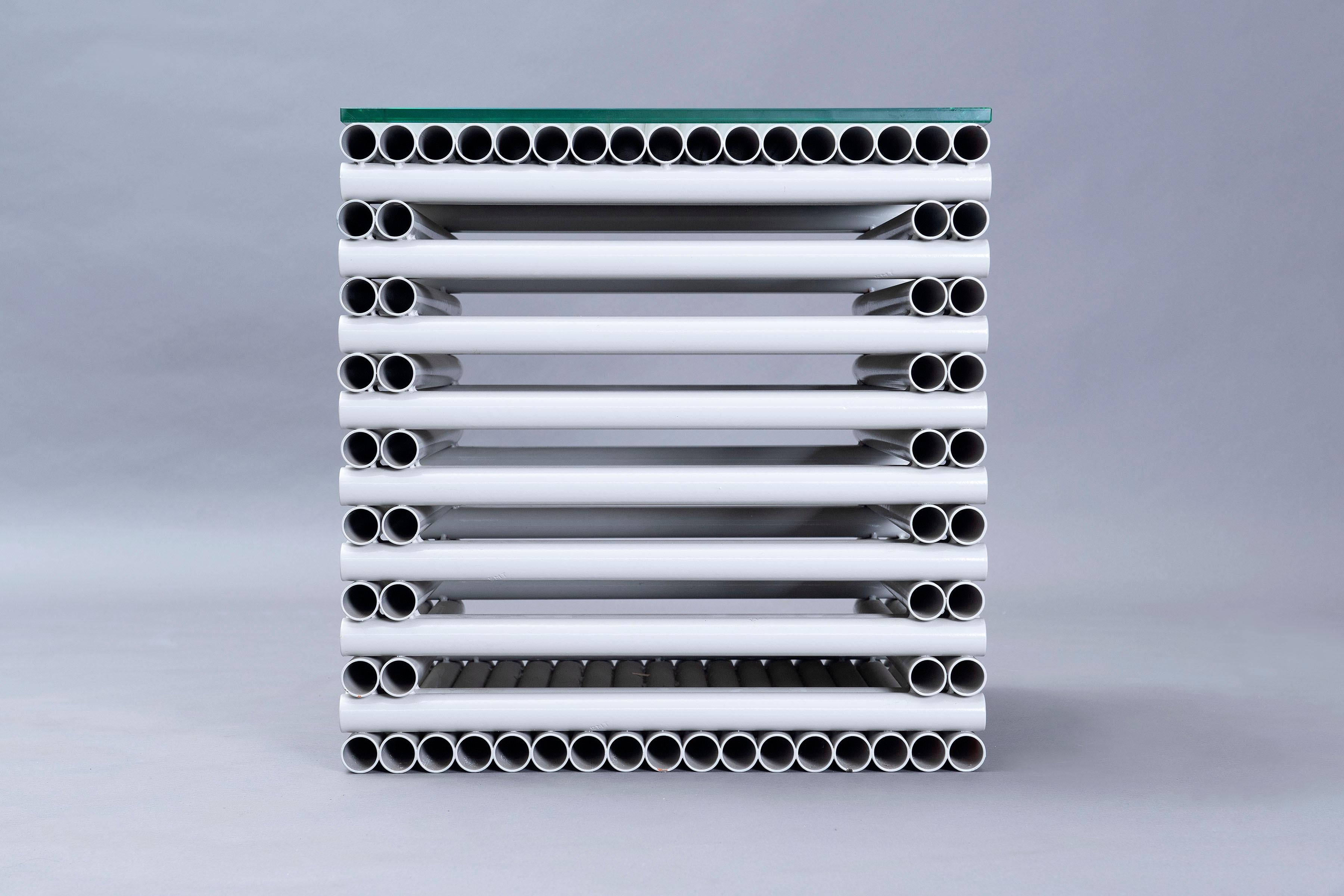 Dieser pulverbeschichtete Stahltisch ist aus Elektroinstallationsrohren gefertigt. Die Glasplatte vervollständigt den skulpturalen Kubus, eine Hommage an Carl Andre, indem sie ihn in ein funktionales Möbelstück verwandelt.