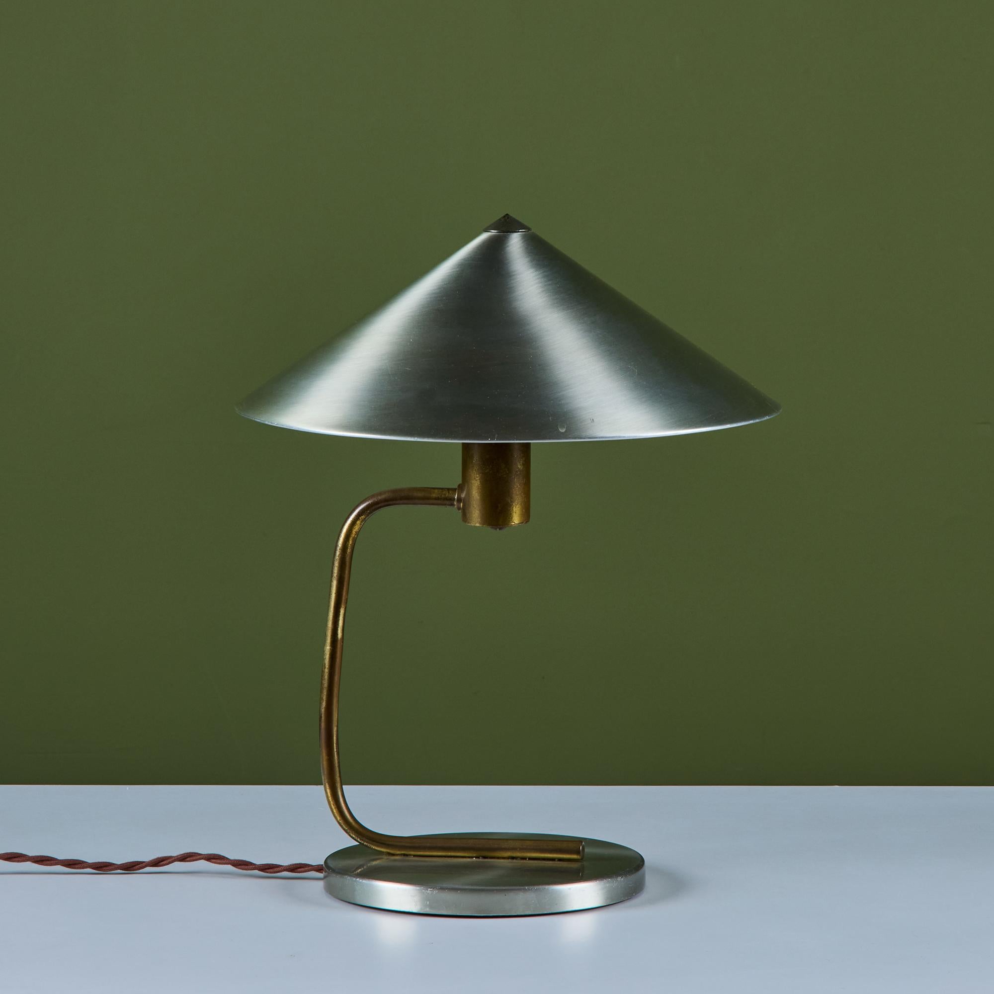 Tischleuchte, entworfen von Walter Von Nessen, ca. 1930, USA. Die Leuchte hat einen kegelförmigen Aluminiumschirm und einen runden Sockel mit einem gebogenen Messingstiel.

Abmessungen
14