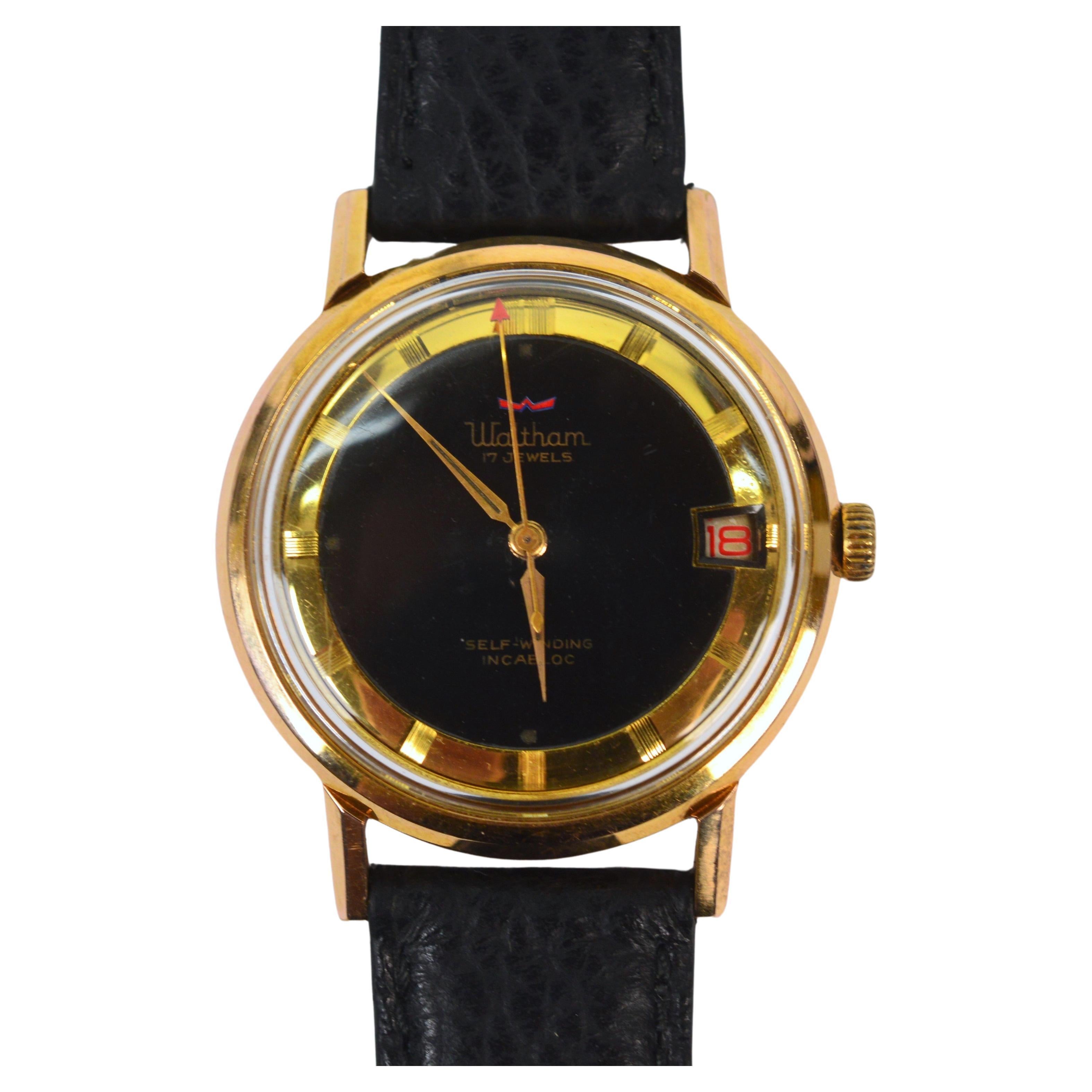In its period and considered modernist style circa late 1950's, this 33mm vintage Waltham Men's Wrist Watch presents a sleek look with a black face,contrasting gold-toned spear hands and understated gold-tone numeral markers. The date window