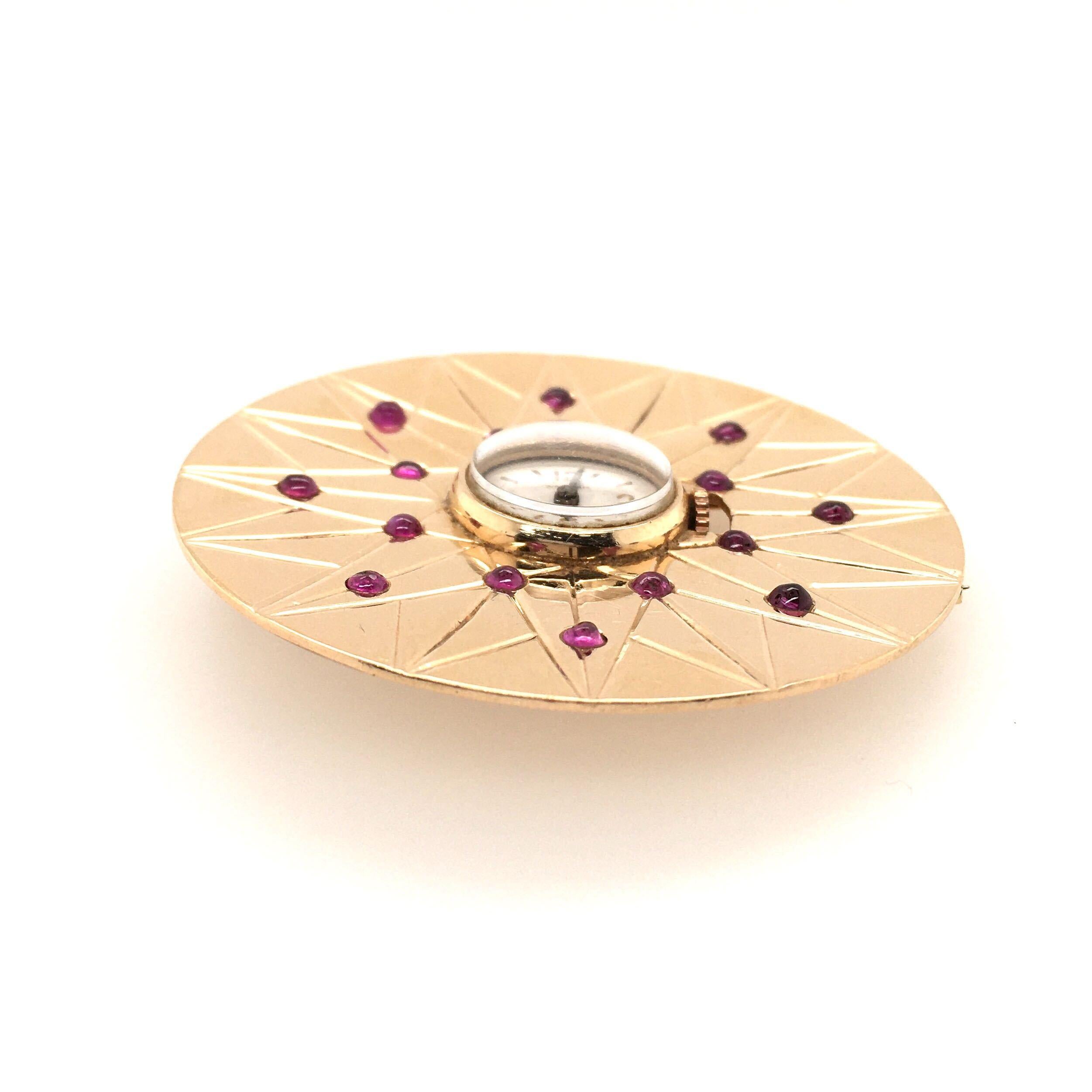 A 14 karat yellow gold and ruby watch brooch. Waltham. Circa 1940. Designed as a polished gold disc, decorated with a star motif, enhanced by small round cabochon rubies, centering a watch, of mechanical movement, 16.5mm, the white dial with Arabic