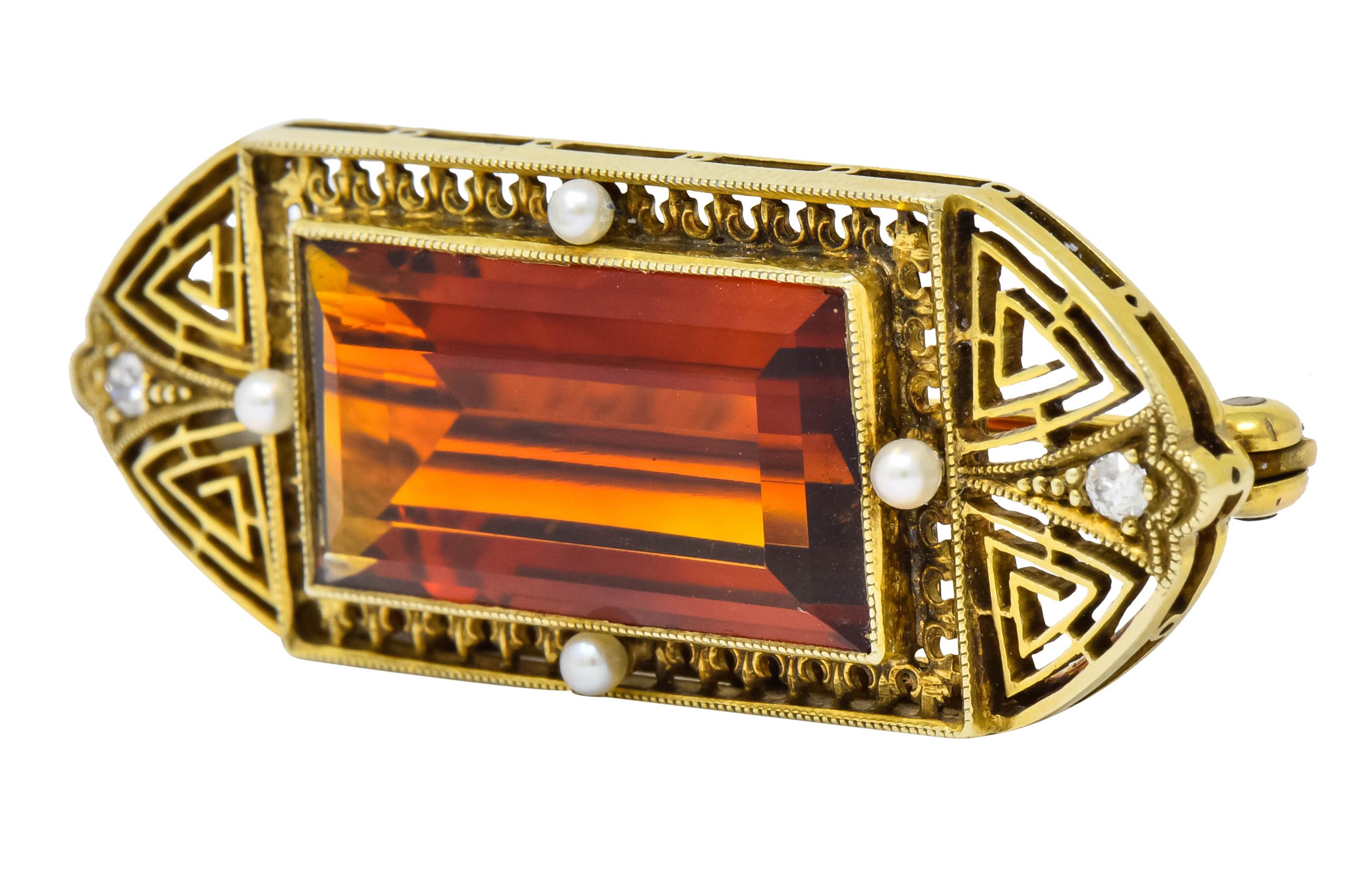 Centering a rectangular step cut citrine weighing approximately 10.41 carats, transparent and a rich medium-dark orange color

Bezel set within a rectangular millegrain frame surrounded by pierced fishtail motif and four round seed pearls

Flanked