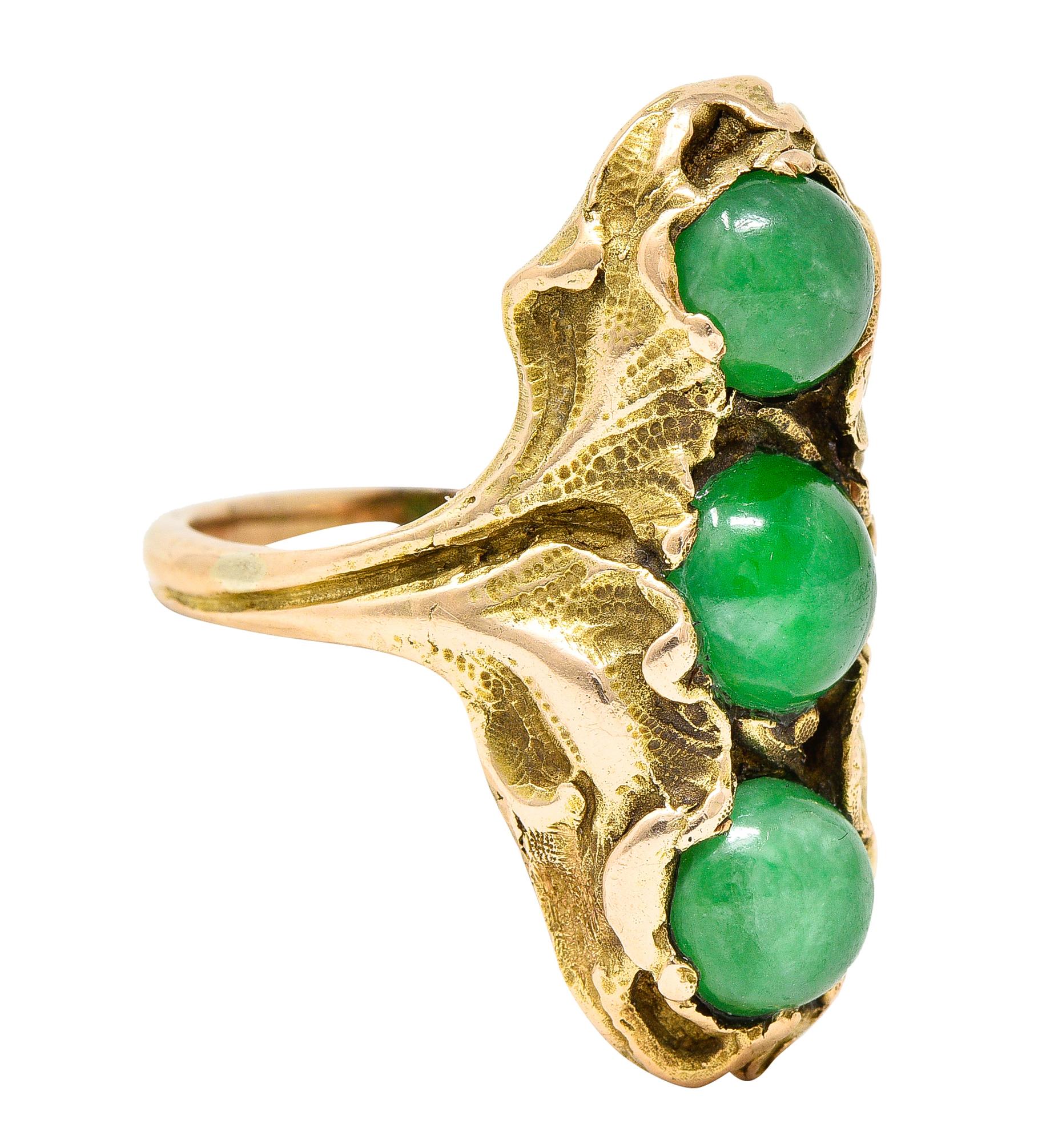 Ring is highly rendered as stylized ginkgo leaf foliate. Encompassing three round jade cabochons. Set North to South while measuring 7.0 mm to 6.0 mm. Translucent and vividly green in color with moderate mottling - good polish. Stamped 14K for 14