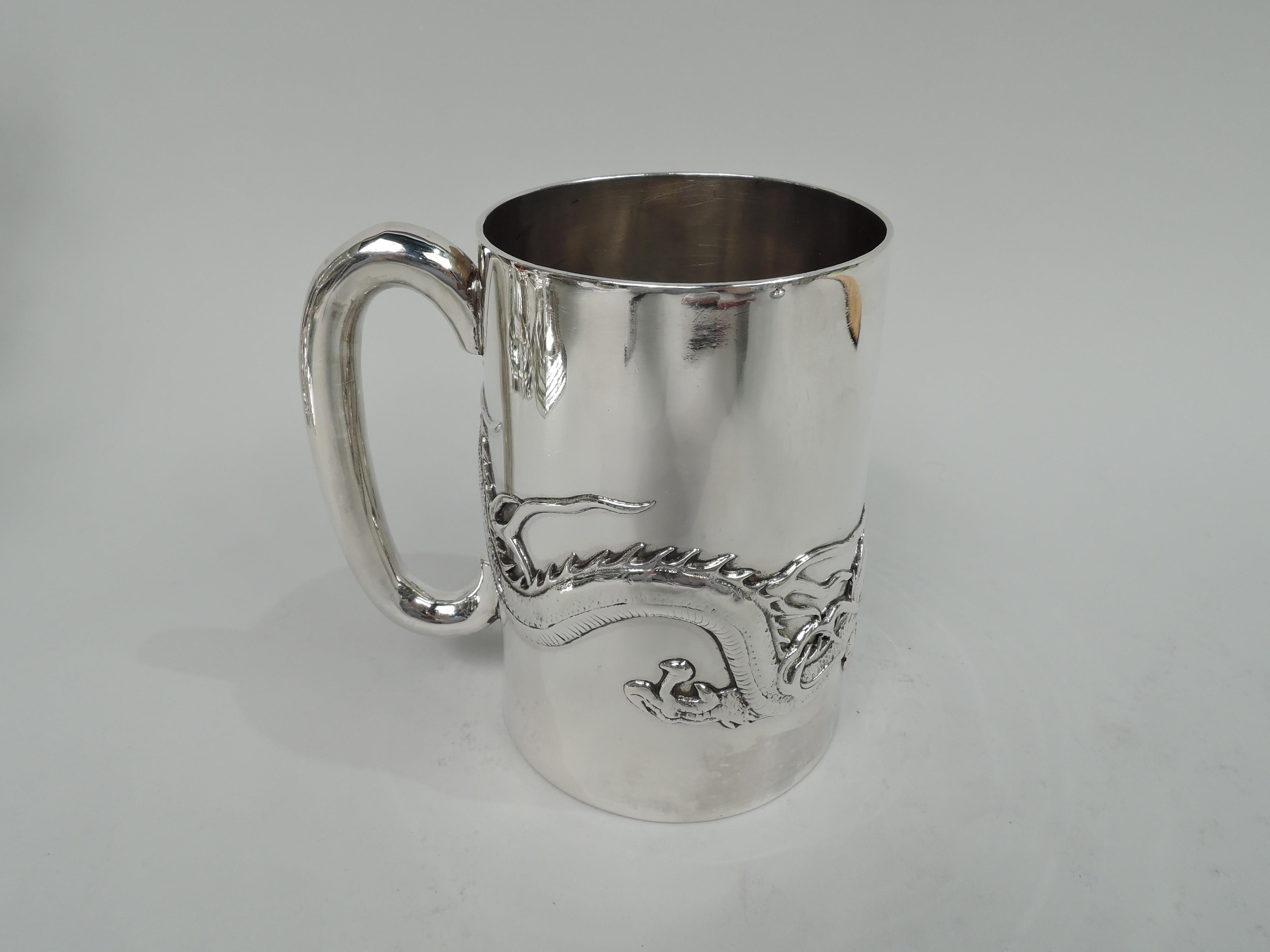 Chinese silver mug, ca 1910. Straight and upward tapering sides and c-scroll handle. A spare form enlivened with applied wraparound dragon chasing its tail. Marks include stamp for Wang Hing, a maker and retailer in Canton and Hong Kong. Weight: