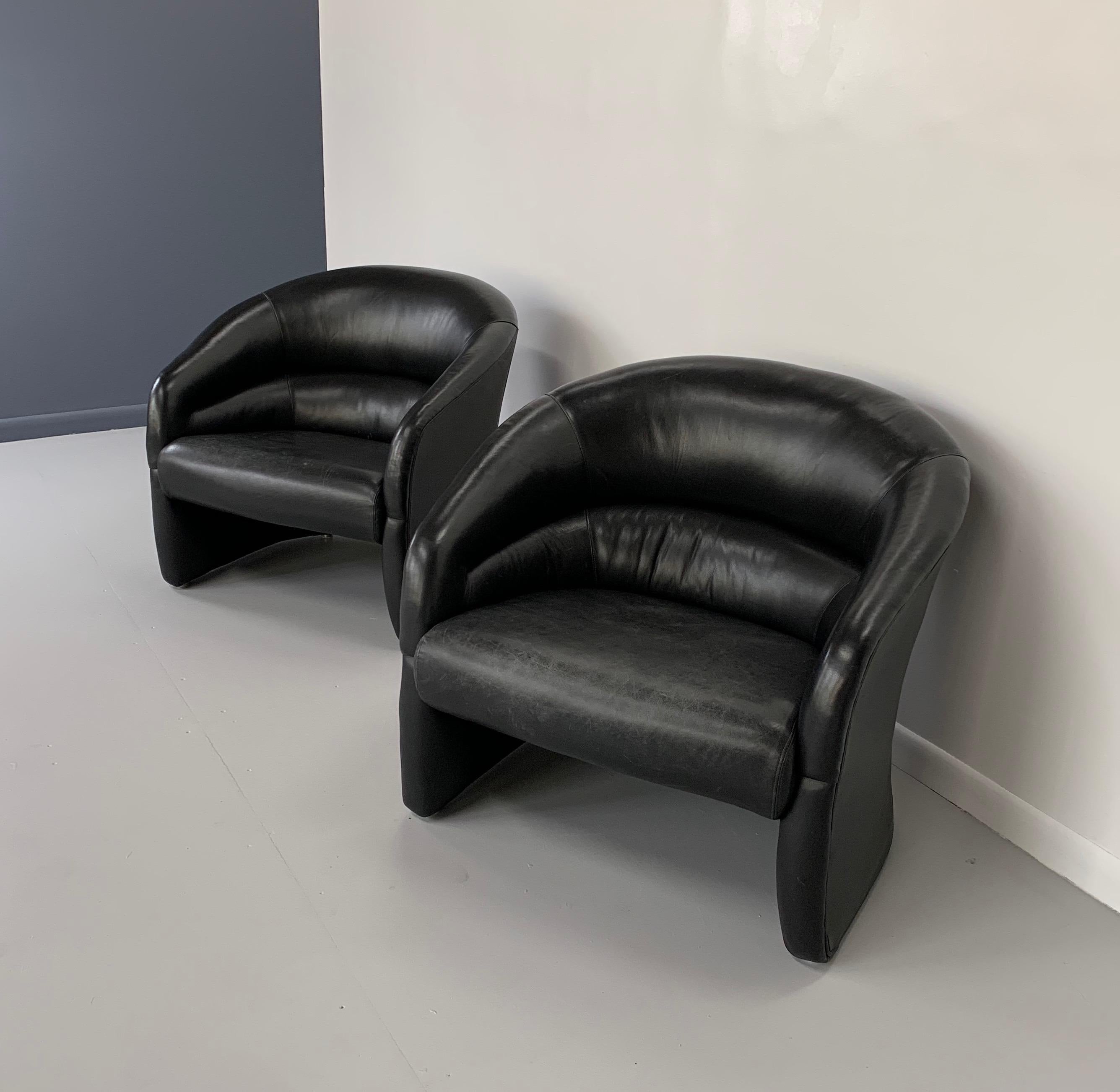 Two pair of black leather barrel back club chairs. These chairs are upholstered in a supple black leather with a pleated back and are very comfortably cushioned.