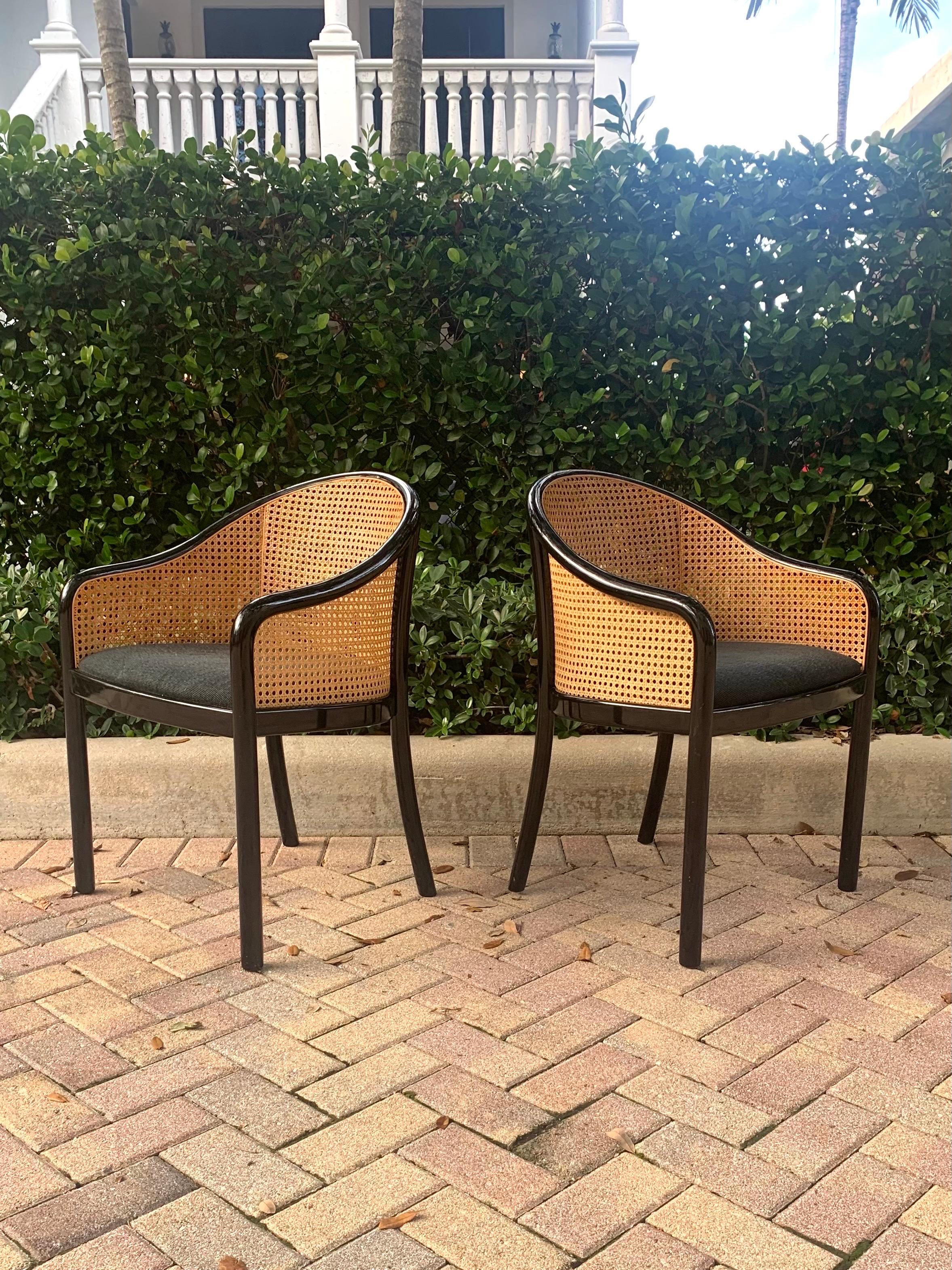 Beautiful pair of chairs based on Ward Bennett’s Landmark chair. In black lacquered wood and cane. With an upholstered cushion. Structure and cane are in great shape. 

With its simple flowing shape and cane back and sides the chairs effortlessly