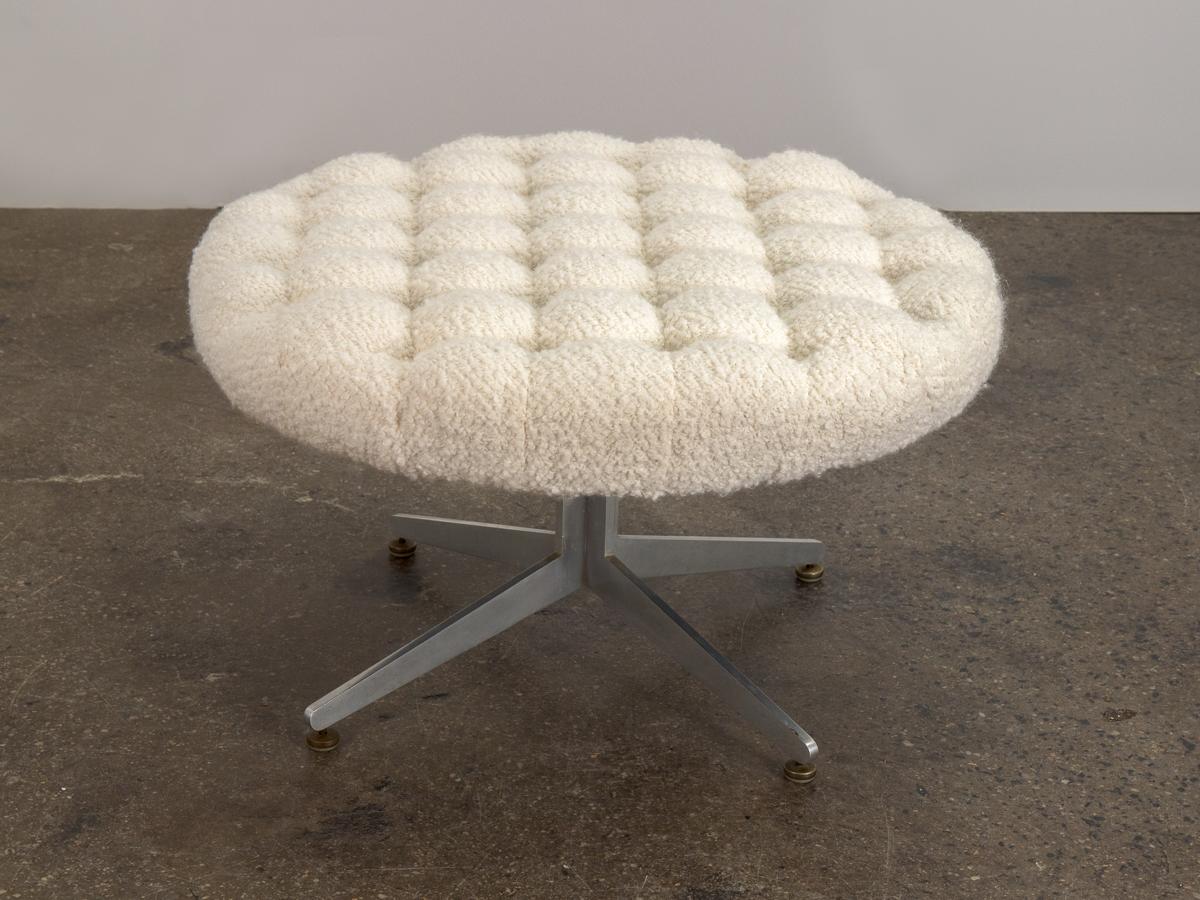 A lovely tufted ottoman designed by Ward Bennett for Lehigh Leopold. Newly upholstered in ivory bouclé fabric that contrasts nicely with brushed aluminum base. This sizable ottoman swivels at the base, adding function to its textured elegance. USA,