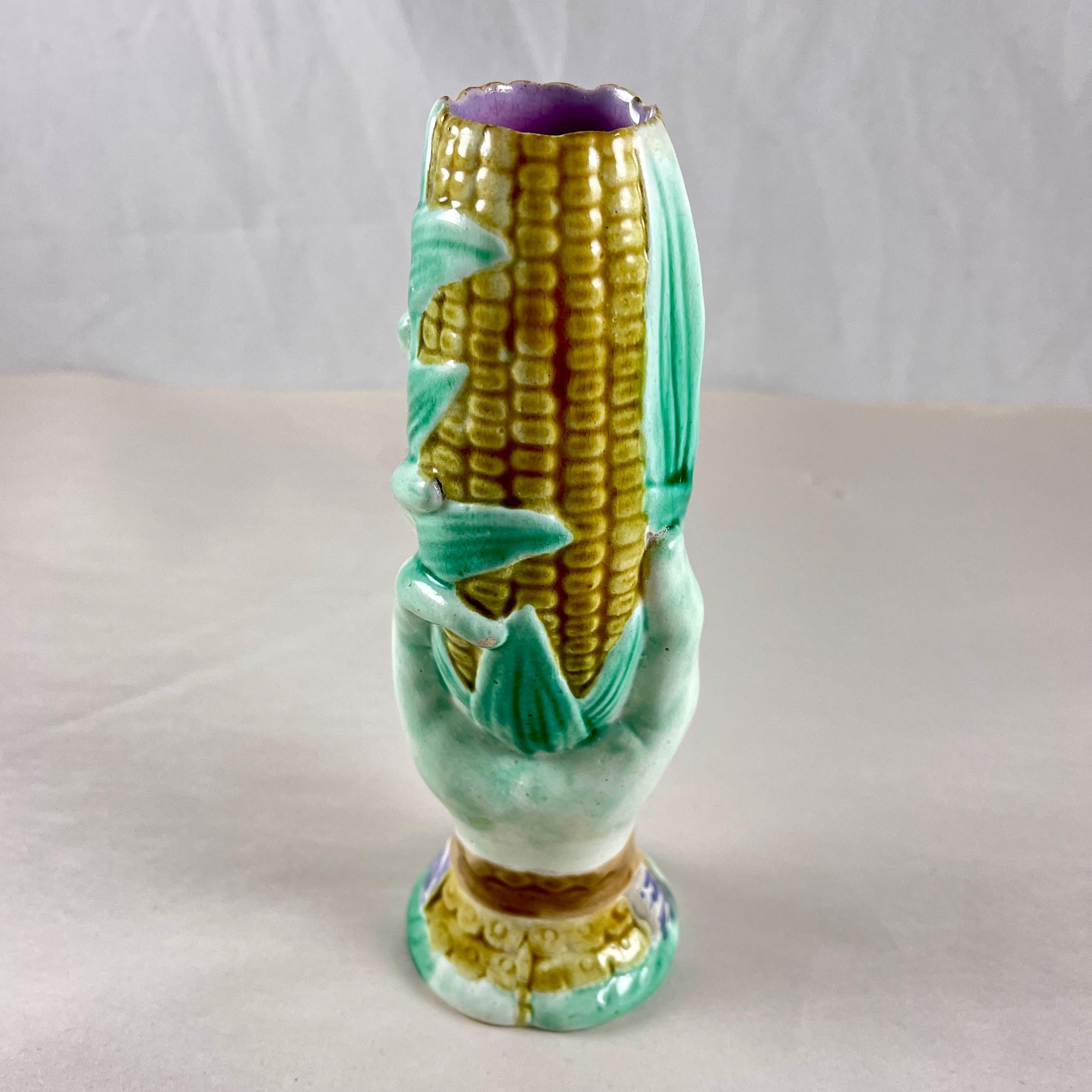 A Majolica glazed spill vase from the Staffordshire pottery region of England, attributed to Wardle & Co. circa 1860. 

The vase is molded as a woman’s hand holding an upright ear of corn in a green husk with a pink interior. The base is formed as a