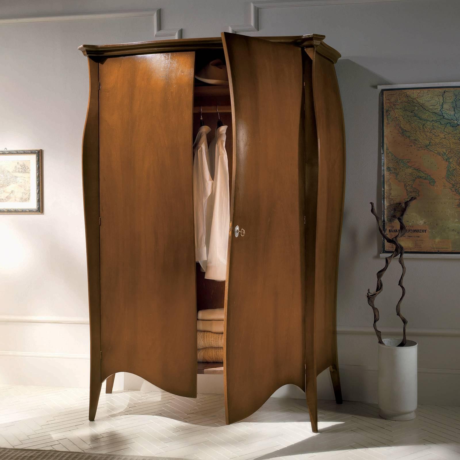 Stately and versatile, this wardrobe is a striking addition to a master bedroom decor. The voluminous, three-dimensional structure is characterized by a sinuous facade, scalloped lower edge, and delicate trim accents. Flanking the two front sides of