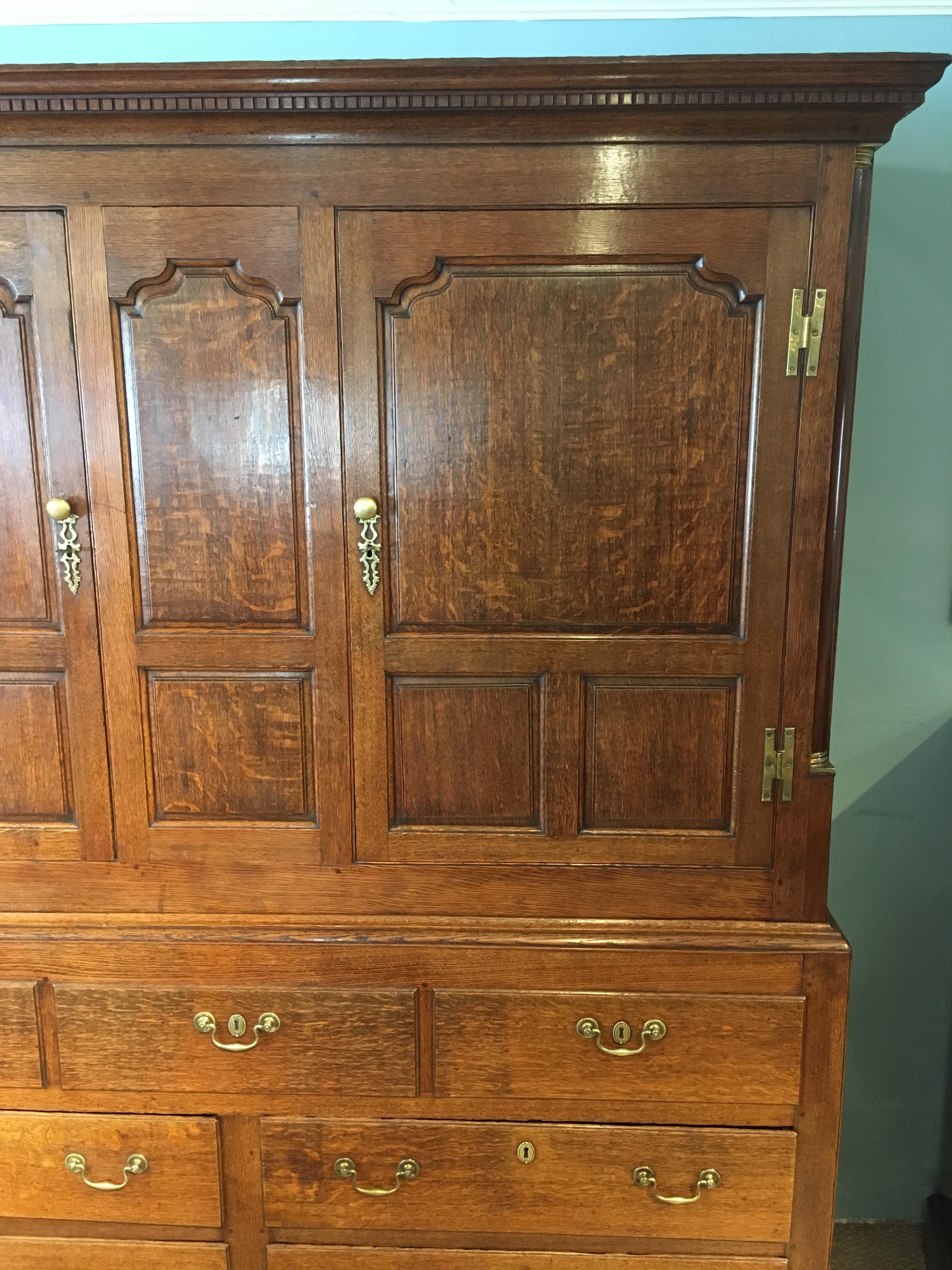 English oak hall cupboard, wardrobe, circa 1870, the two cupboard doors opening to reveal the hanging space, three false drawers over four drawers. 


Fielded paneled doors, original brass H hinges standing on ogee bracket feet, mahogany