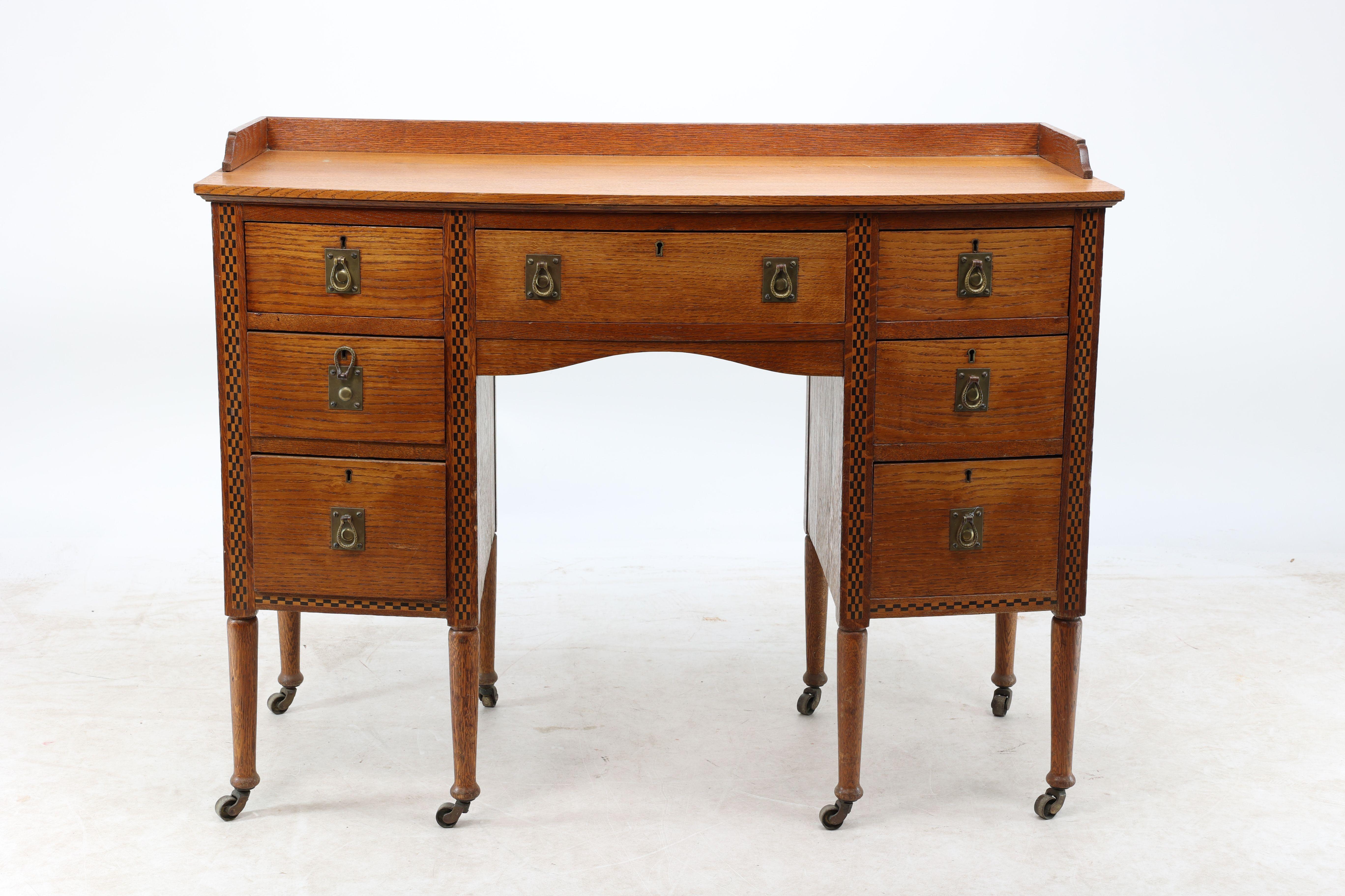 Waring et Gillows attribués. Bureau de style Arts and Crafts à double piédestal avec incrustation en damier et poignées en laiton martelé à la main, pieds tournés sur roulettes d'origine.