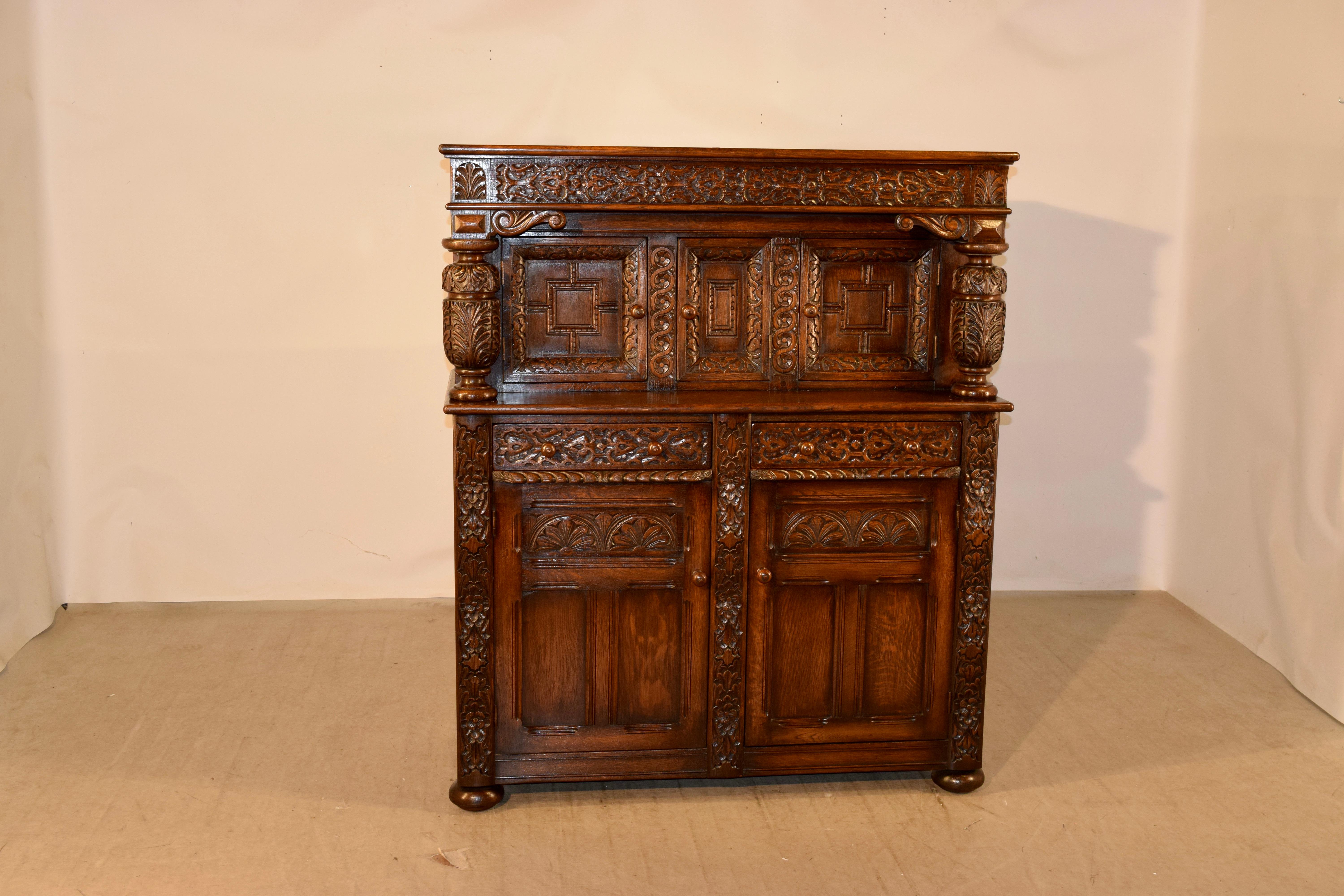 Circa 1900-1909 English oak court cupboard by Waring & Gillow. This cupboard is of tremendous quality and has a heavily carved case. The upper molding is heavily carved and is over three paneled doors, which open to reveal storage. There are two