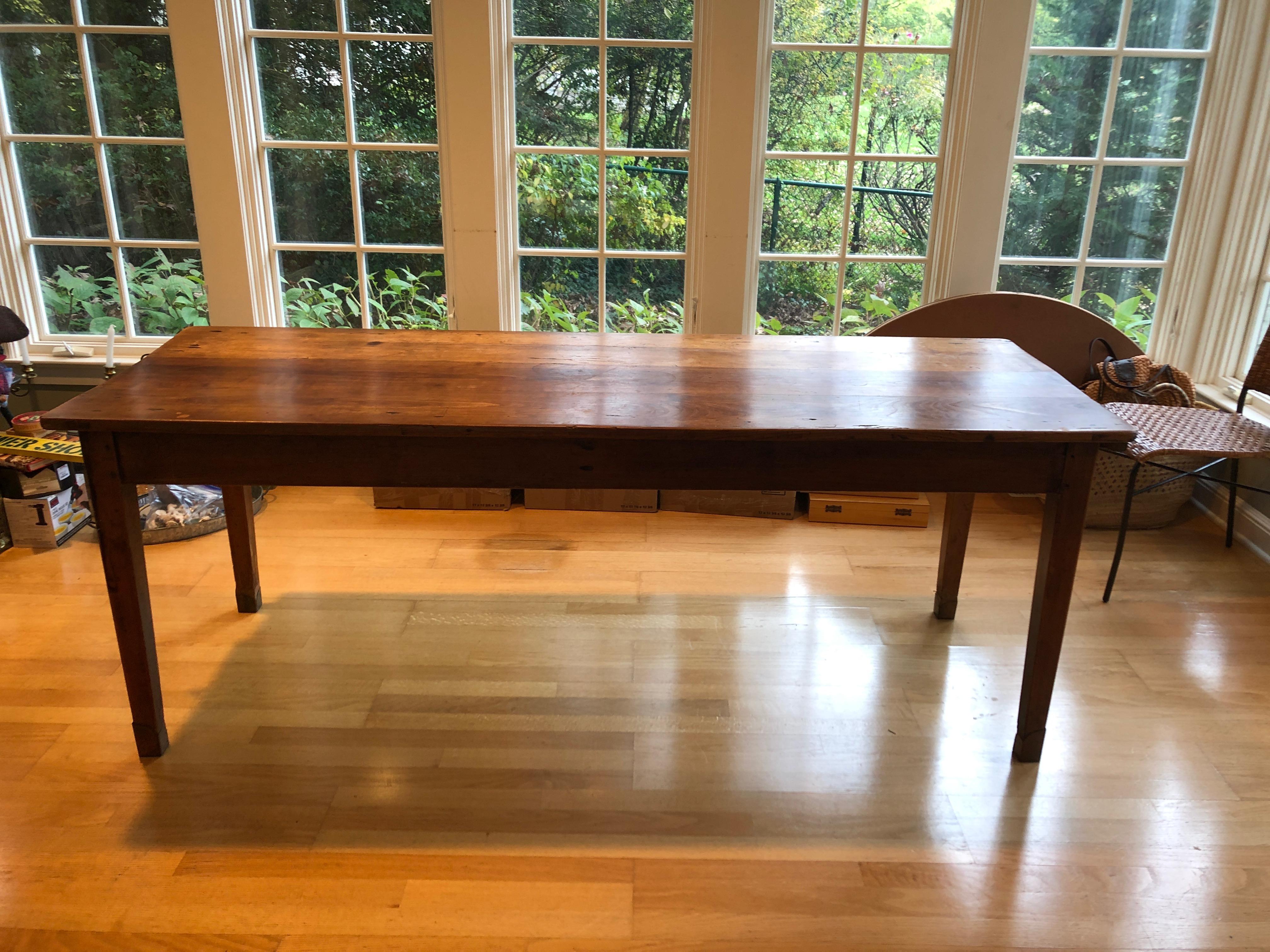 A warm and friendly antique cherry farm table having plank top, extendable rustic breadboard on one end and single drawer on the other, elegant tapered legs with brass caps.