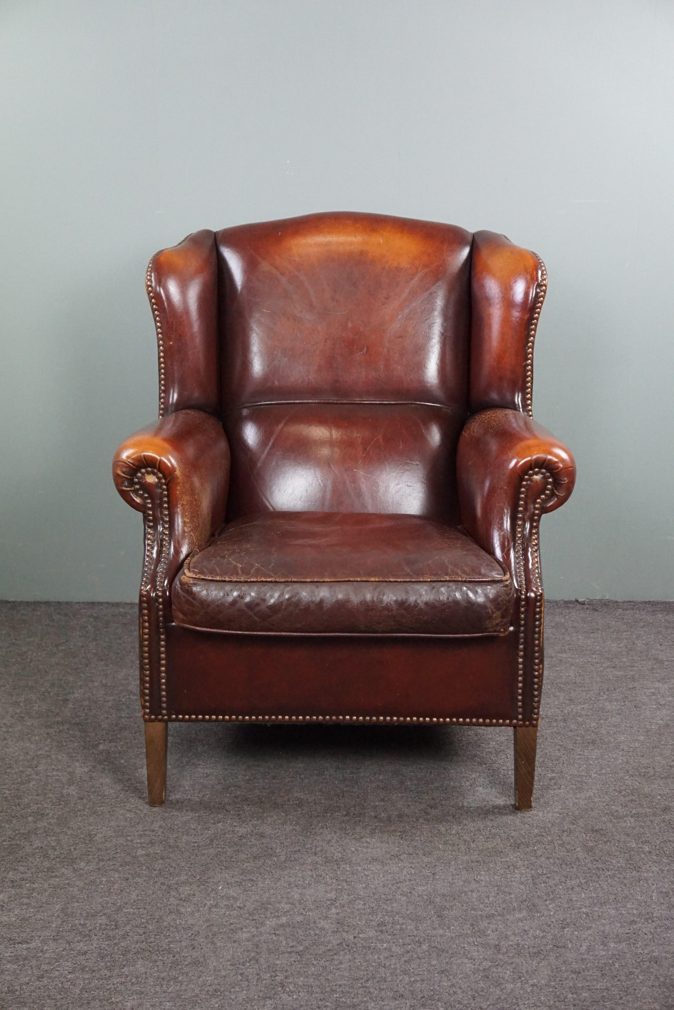 Offered is this beautiful warm-colored sheep leather wing chair finished with beautiful decorative nails.

This armchair has a strikingly beautiful warm brown/red color and a beautiful patina. The surface division in the backrest and the decorative