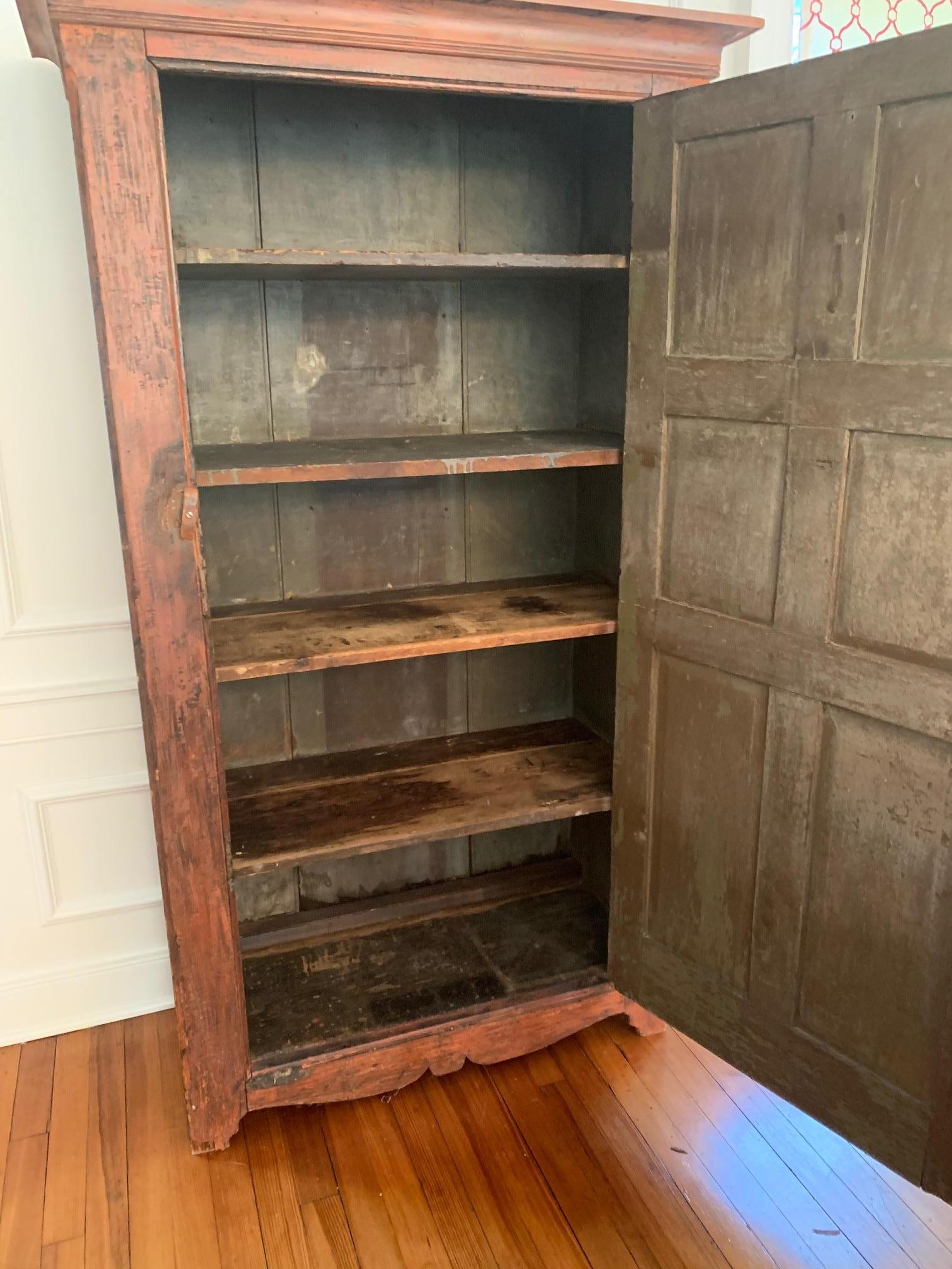 A wonderfully functional and home warming distressed painted cupboard having fantastic rusty orange paint with brown undertones and lots of storage inside.