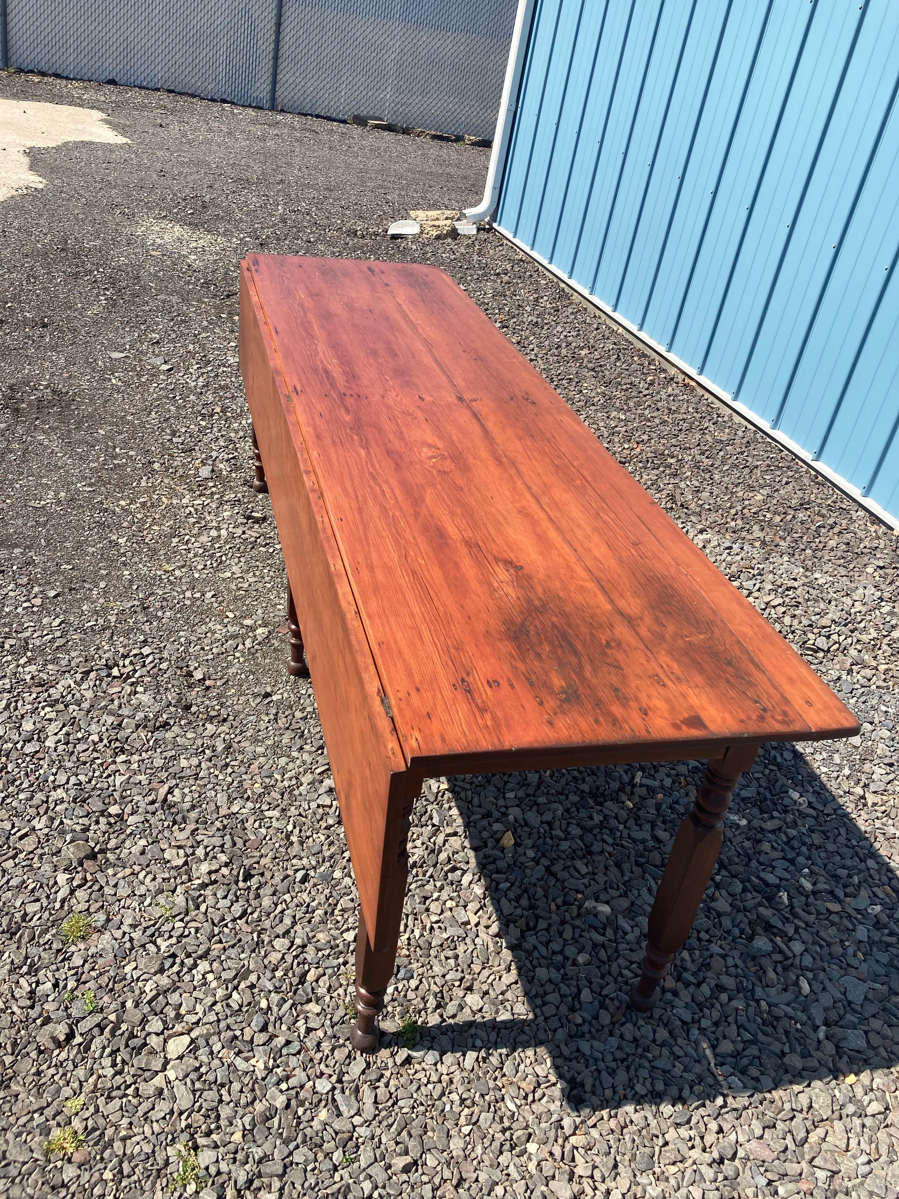Impressive and character rich antique drop leaf harvest table, circa 1860, having maple turned legs and a Canadian pine top. 
 Measures: 25 3/8” wide with leaf down, 38 1/2” wide with leaf extended.