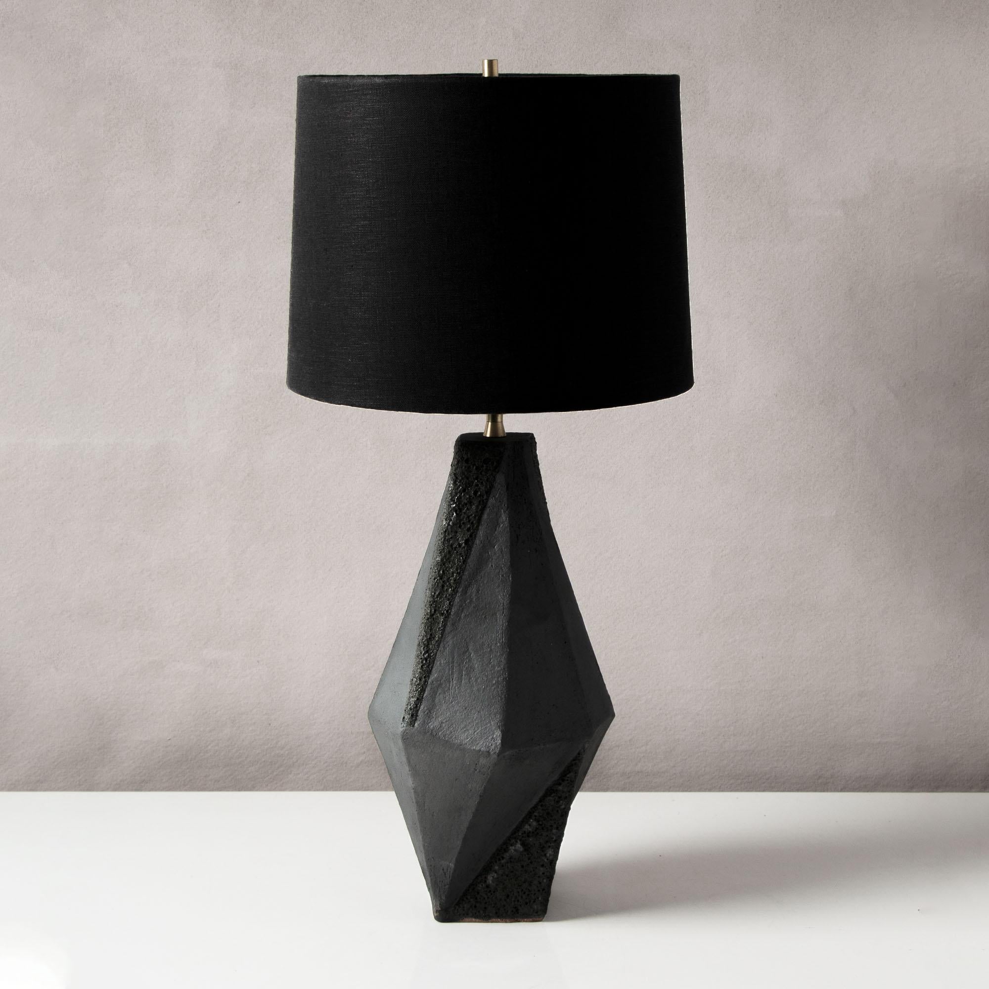 This dramatic ceramic table lamp features a complex geometric shape, accentuated by contrasting matte white and textured black glazes. Each piece is individually handmade and entirely unique. 

Available in two colors, with a white or black linen