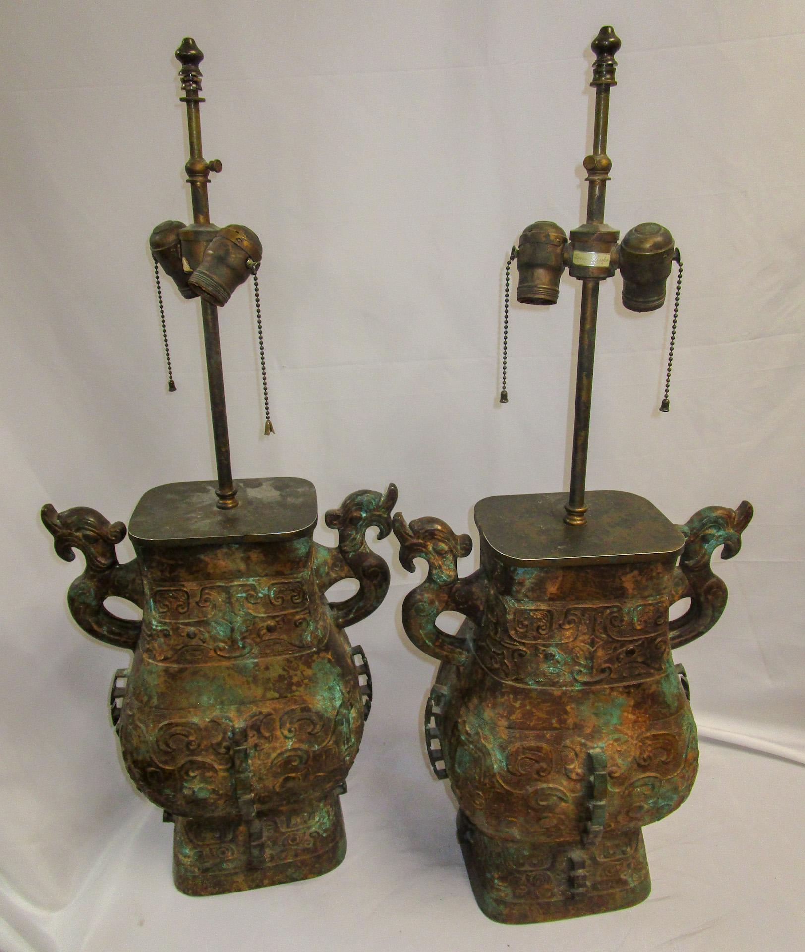 Dieses hübsche Paar Bronzelampen weist eine Grünspan-Patinierung auf geätzten Körpern auf, die einen archaischen asiatischen Stil imitieren, sowie zwei drachenförmige Schlaufengriffe und elektrische Doppelleuchten aus Messing,  Das Papieretikett