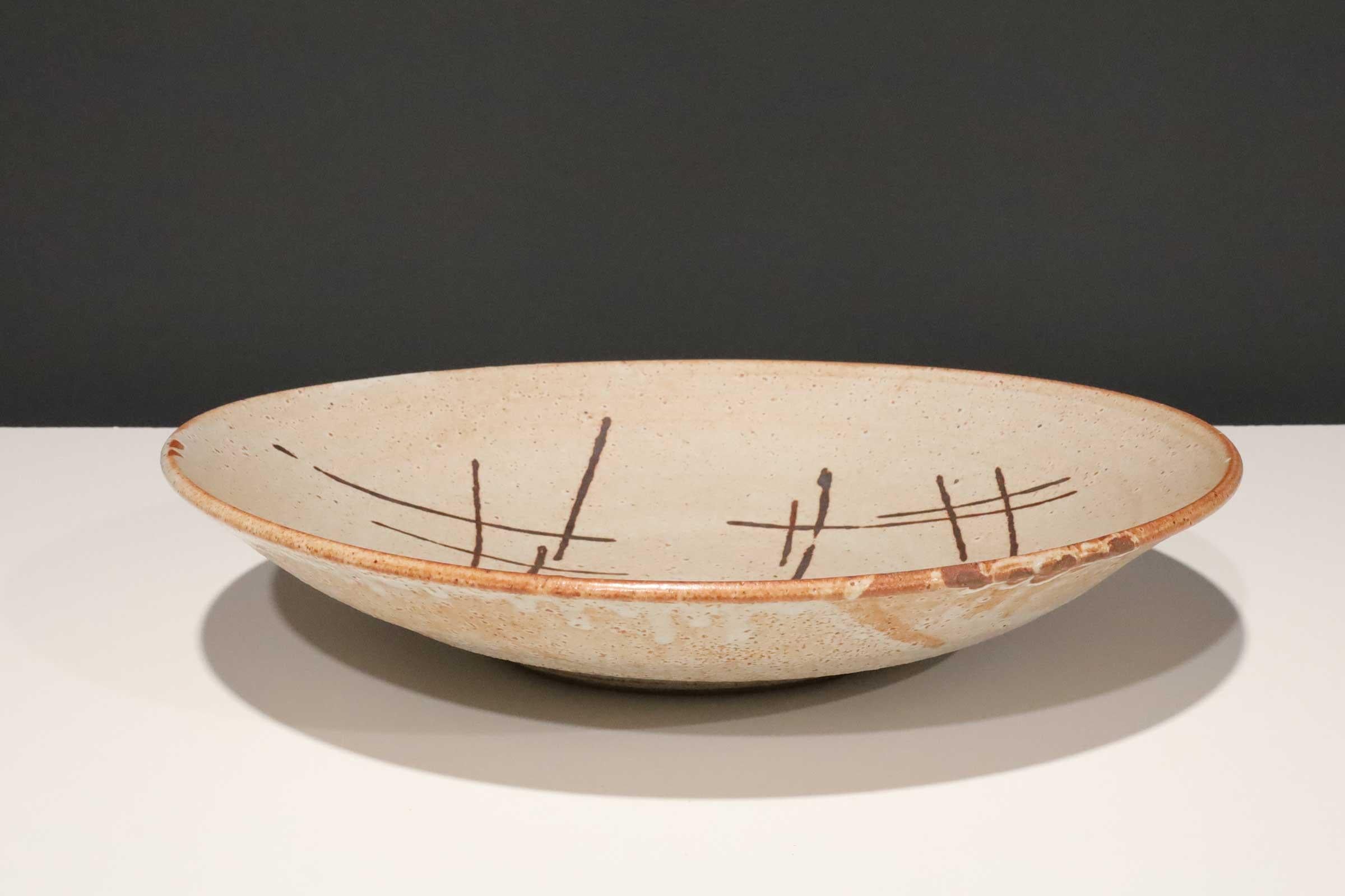 Large studio pottery platter with brown decorative dashes. 

Warren MacKenzie is known for simple, wheel-thrown functional pottery influenced by Bernard Leach and the Japanese aesthetic of the work of Shoji Hamada.

In 1950 MacKenzie and his
