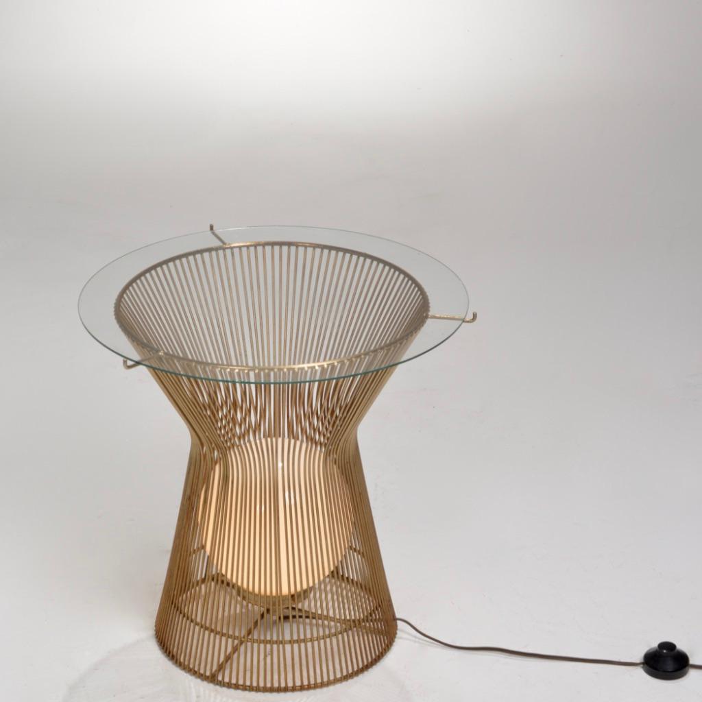 This Warren Platner style side table features a round caged brass-tone steel rod exterior with a globe base light and glass top. This gracefully decorative table serves as both structure and ornament. 
The structure features vertical steel wire