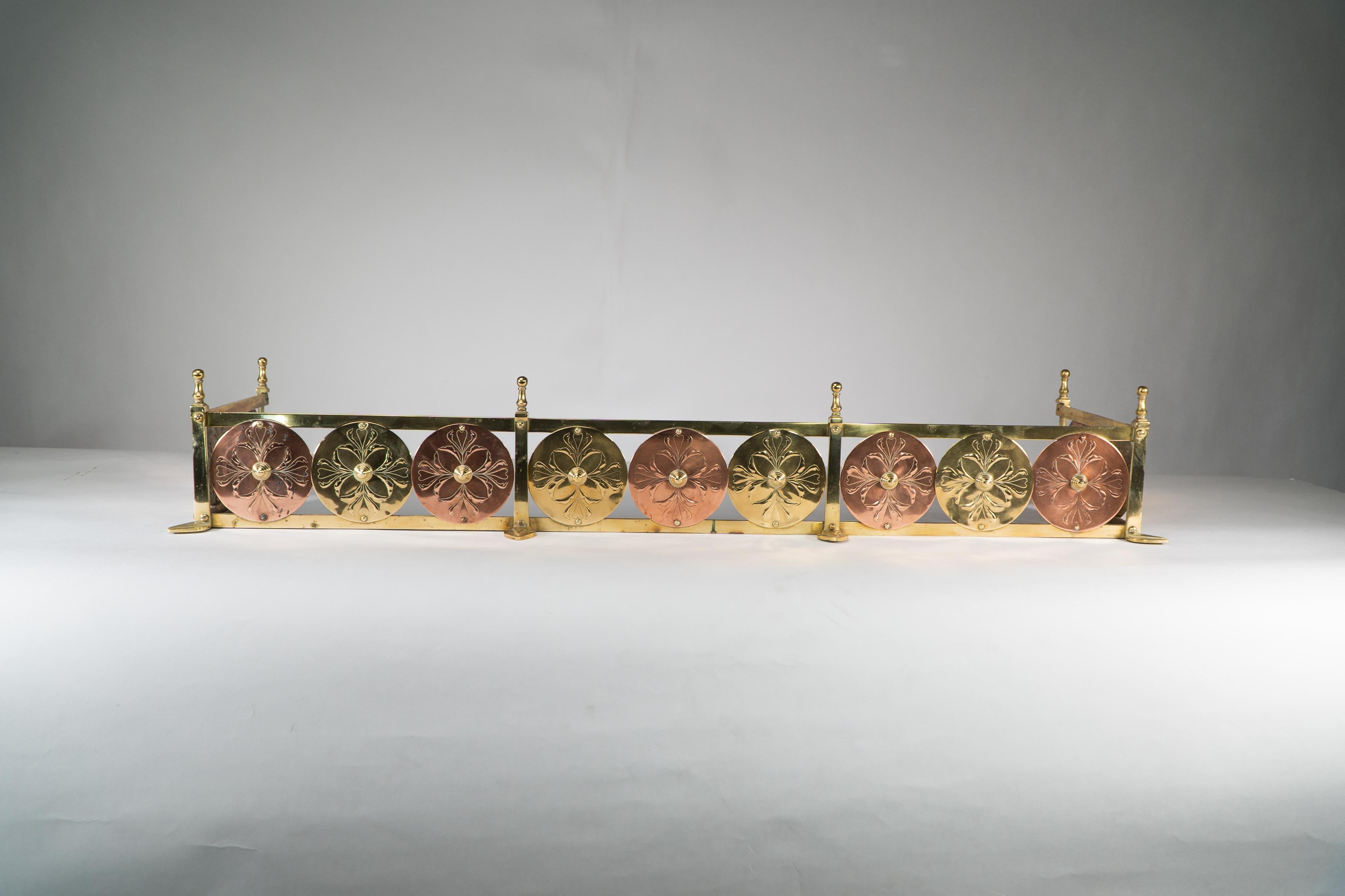 William Arthur Smith Benson and Heywood Sumner. A rare and probably unique Arts & Crafts brass and copper fireplace fender surmounted with six finials and six leaf-shaped feet. The main body with alternating brass and copper discs, each with