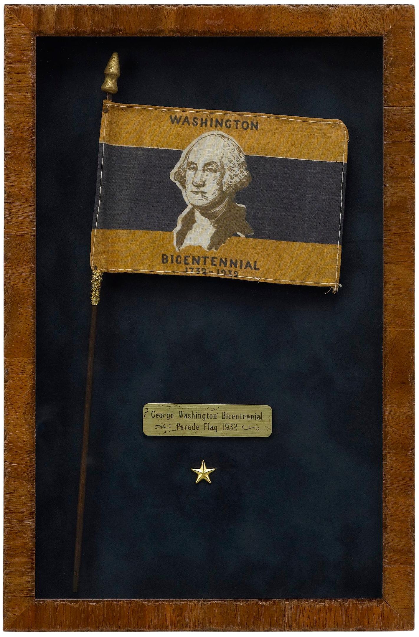 Viene presentata una bandiera da parata del Bicentenario di George Washington del 1932. La bandiera è stampata a strisce d'oro, bianche e blu, con al centro il ritratto del busto di George Washington. Le parole 