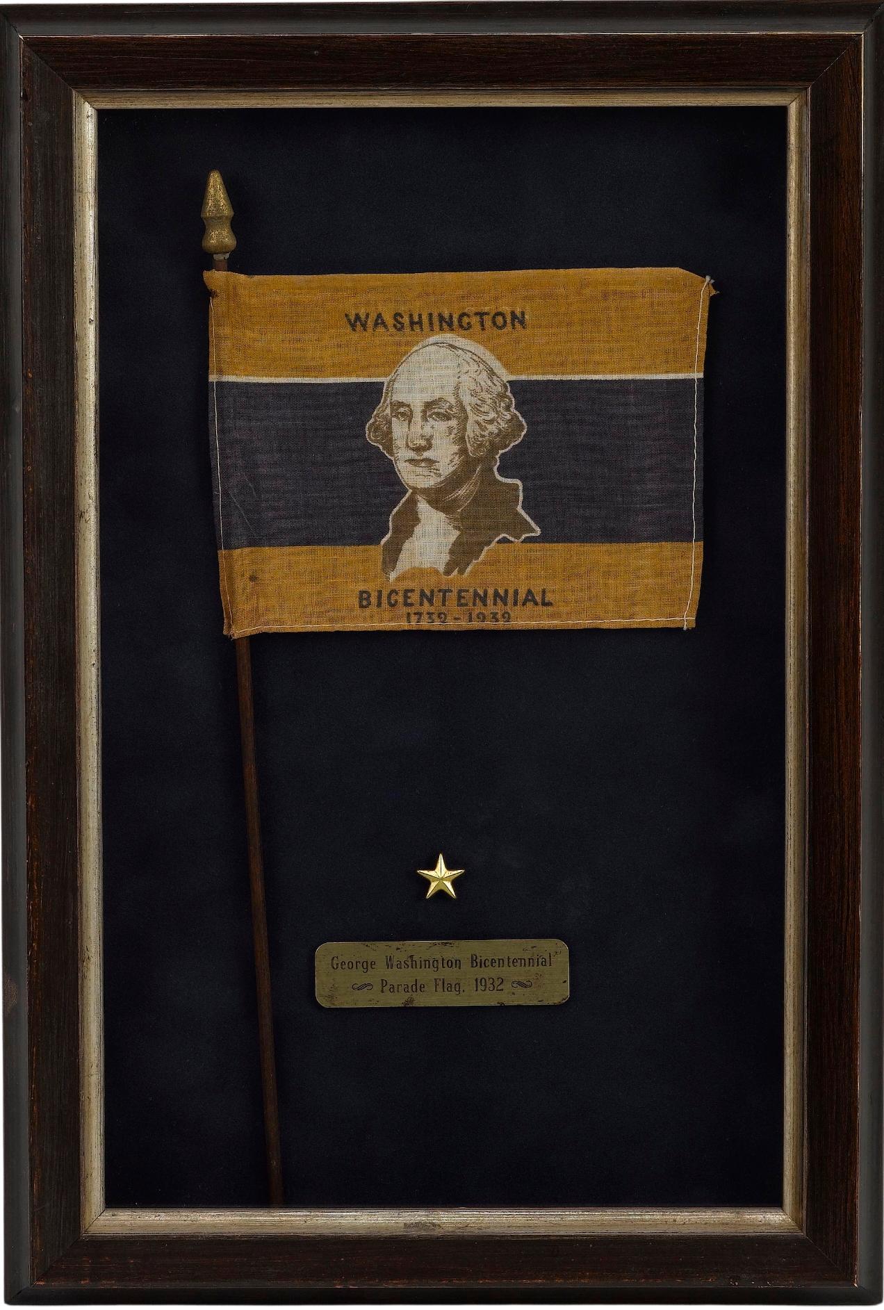 Viene presentata una bandiera da parata del Bicentenario di George Washington del 1932. La bandiera è stampata a strisce d'oro, bianche e blu, con al centro il ritratto del busto di George Washington. Le parole 