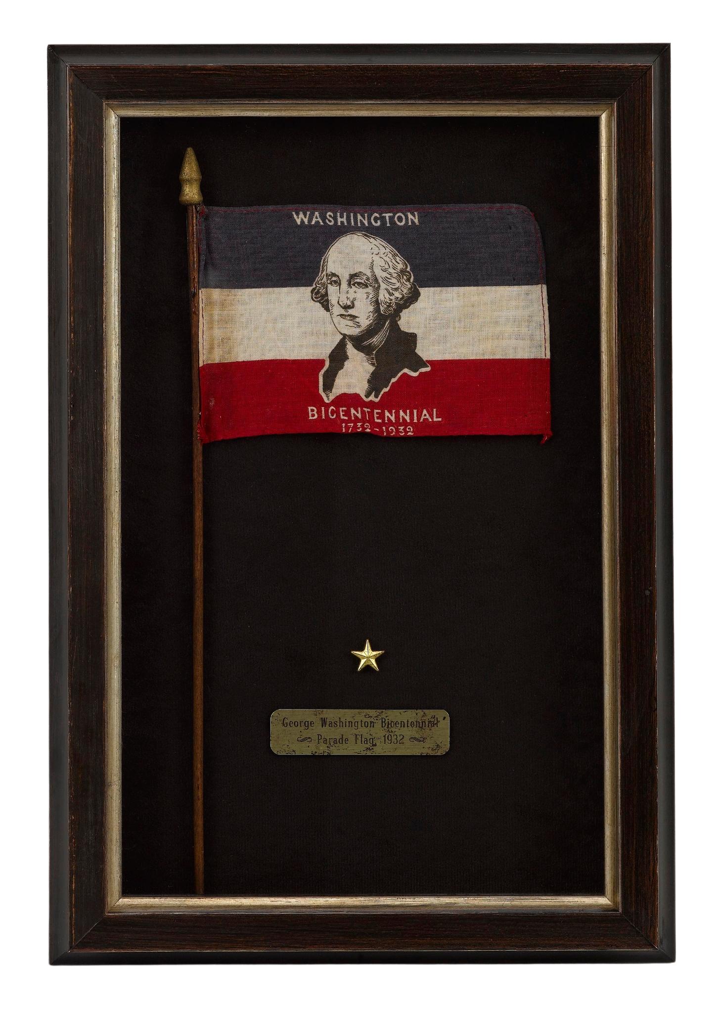 Presented is a George Washington Bicentennial parade flag from 1932. The flag is printed with blue, white, and red stripes, with a prominent bust portrait of George Washington at center. The words “Washington Bicentennial” and the dates “1732-1932