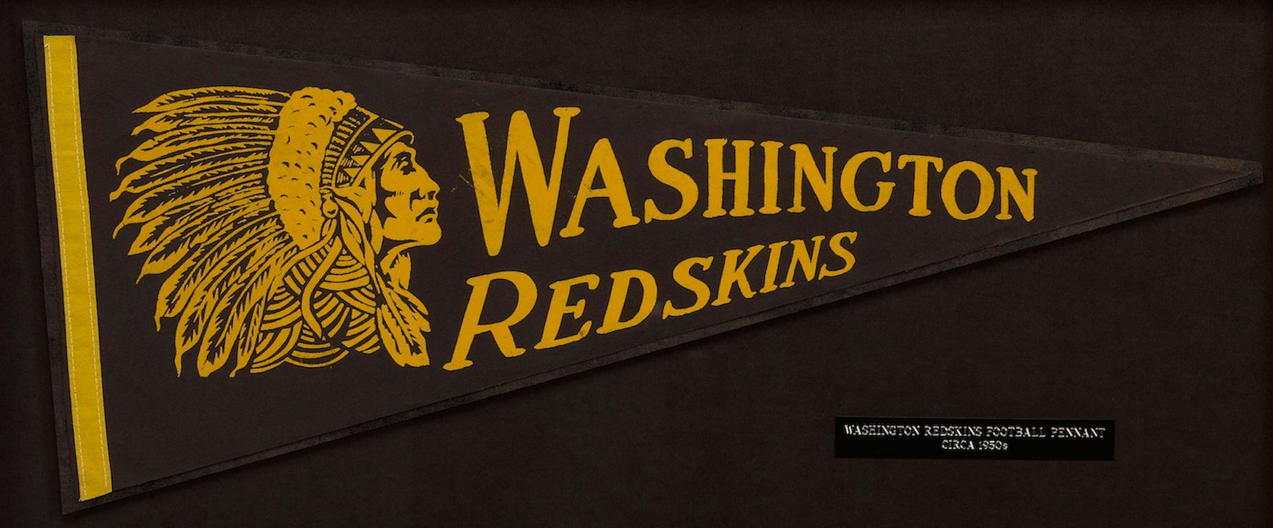 This pennant flag highlights the Washington Redskins football team. The pennant was produced in the 1940s and features the words “WASHINGTON REDSKINS” in bright yellow letters. To the left of the team name is the profile of a Native American man
