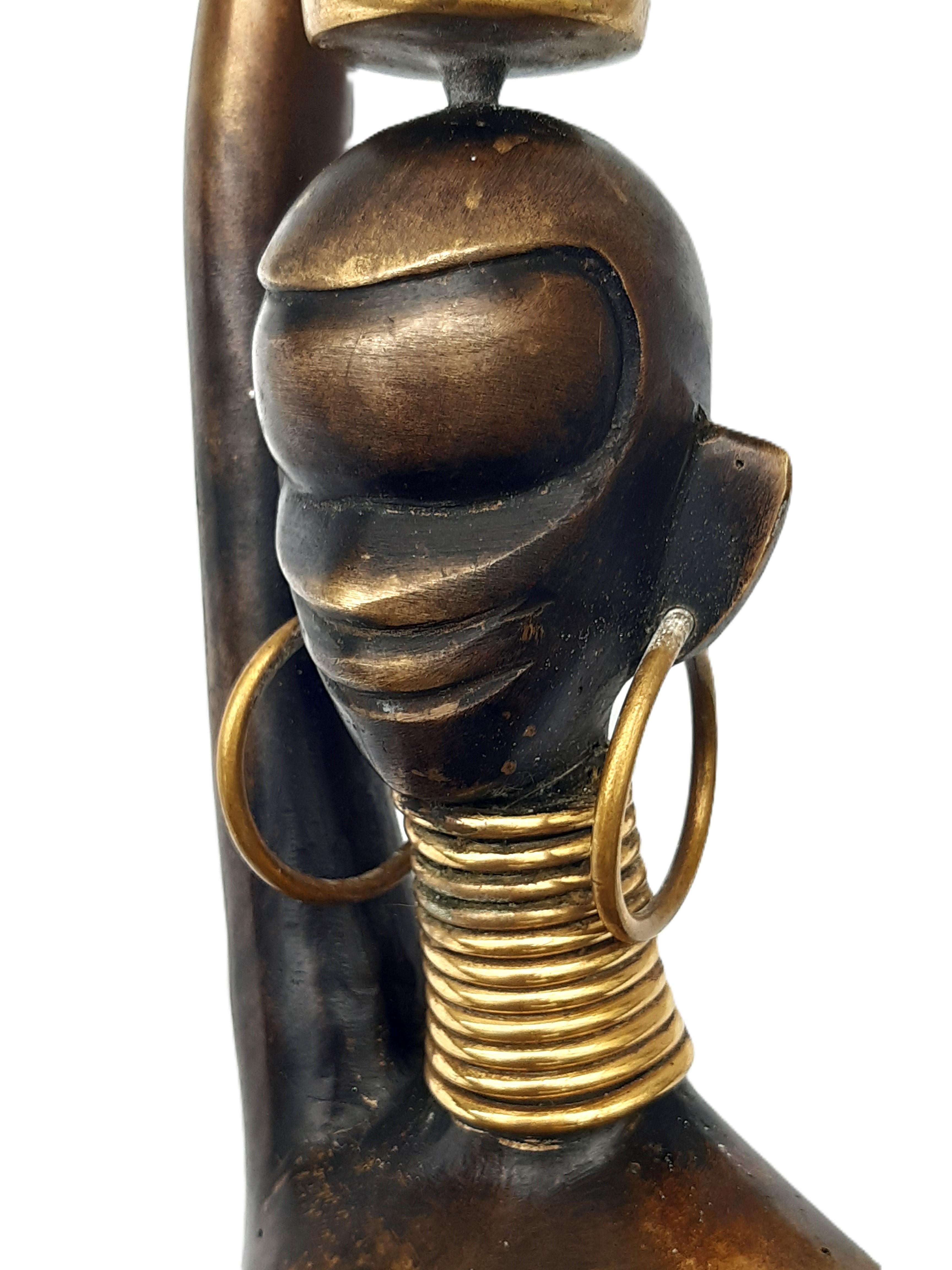 Seltene große Figur einer stlisierten Nubierin (Ndebele), wohl Wien 1950er Jahre, ungemarkt, der Messingguss partiell schwarz und golden patiniert, als Wasserträgerin mit Reifenschmuck.
Con un'altezza di 98 cm si inserisce perfettamente in molti