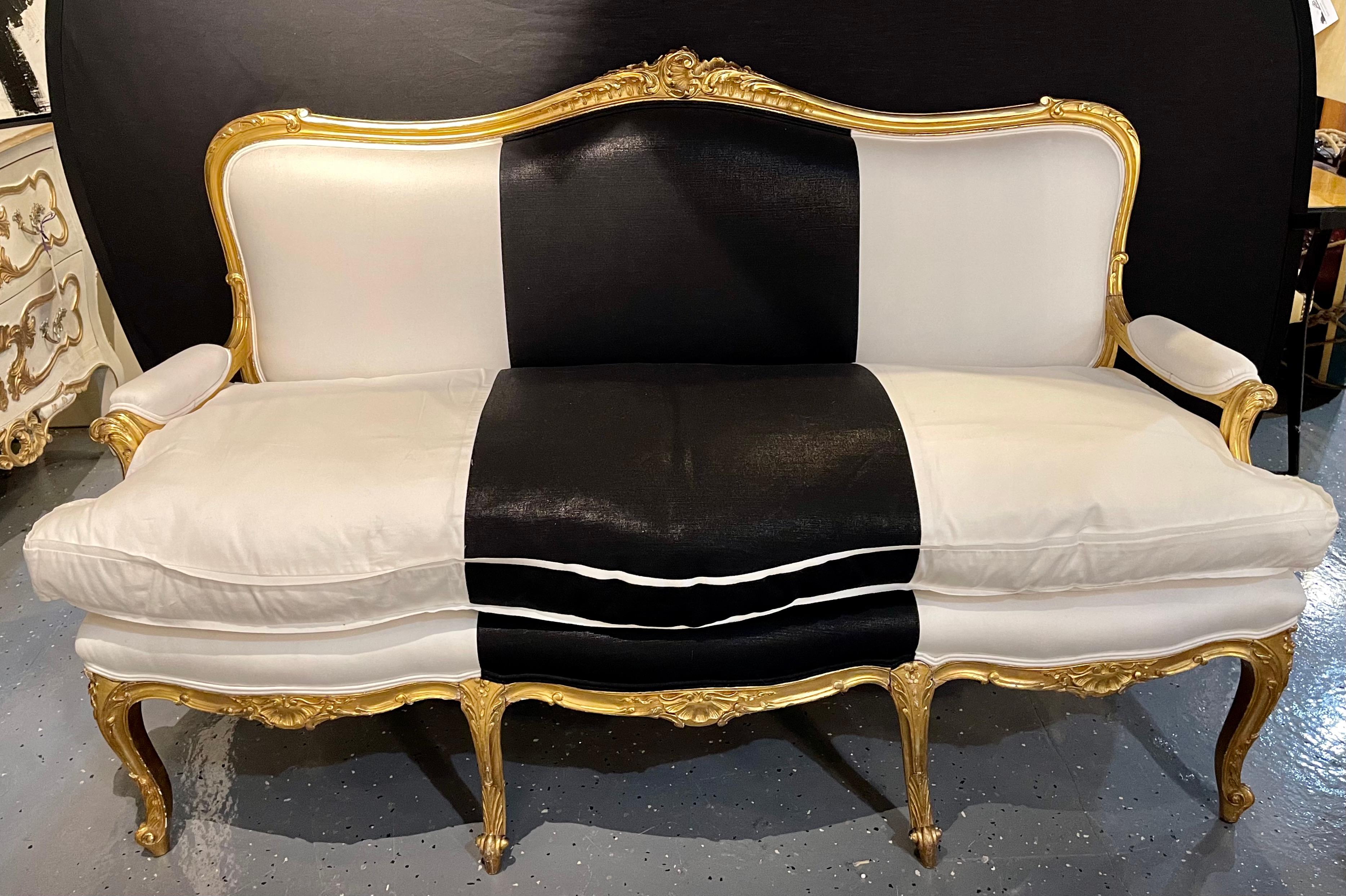 1930s French gilt wood upholstered settee, canape or sofa in black and white polished cotton. One of a compatible pair of finely carved and detailed water gilt decorated Louis xv style canapes or loveseat sofas.
A simply stunning compatible pair