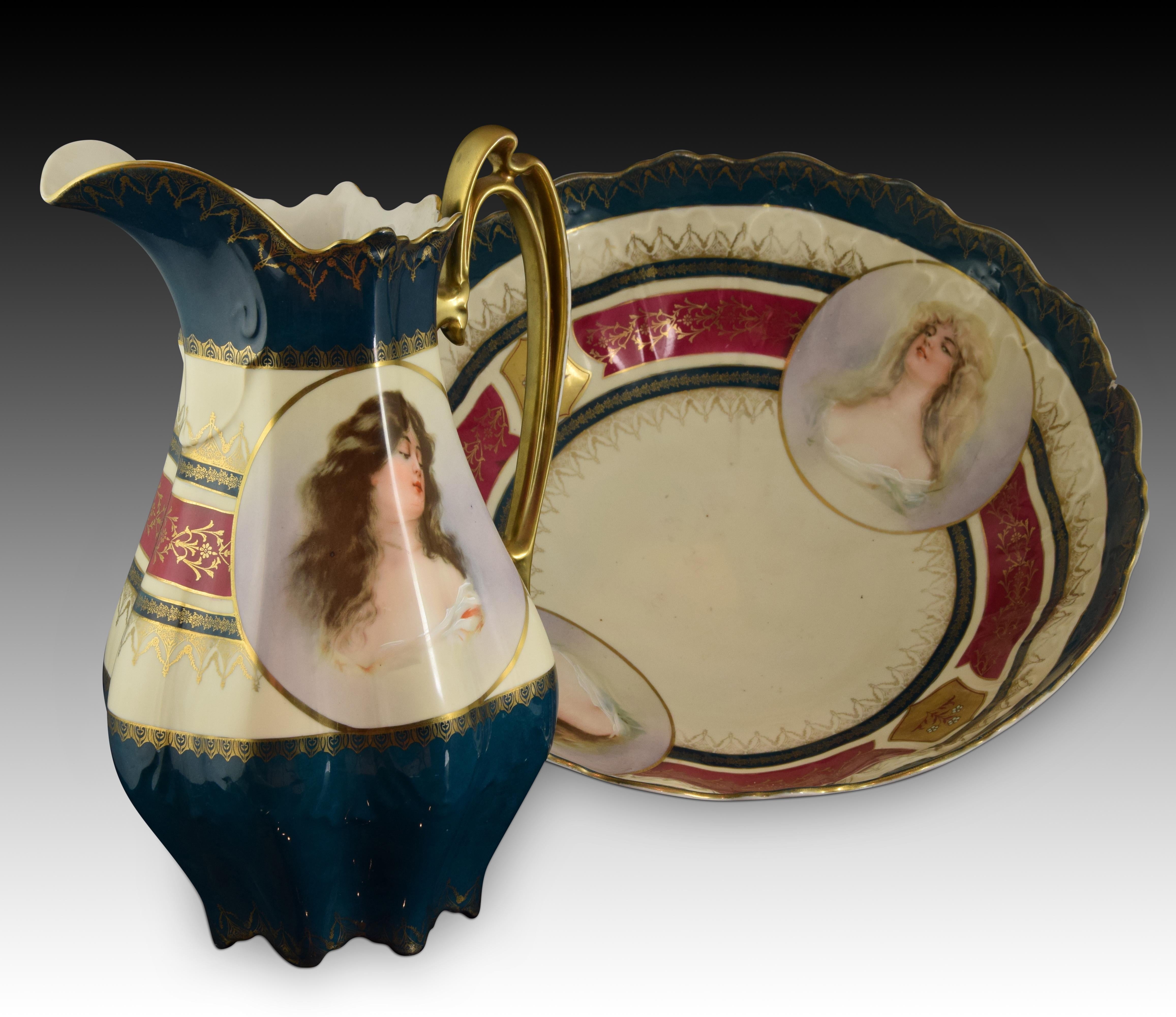 Porcelain. With marks.
Water pitcher set decorated with stripes with floral elements in floral in vivid blue, red and gold tones. The center of the ewer presents a feminine figure, present in numerous works of the factory and painted by hand, that
