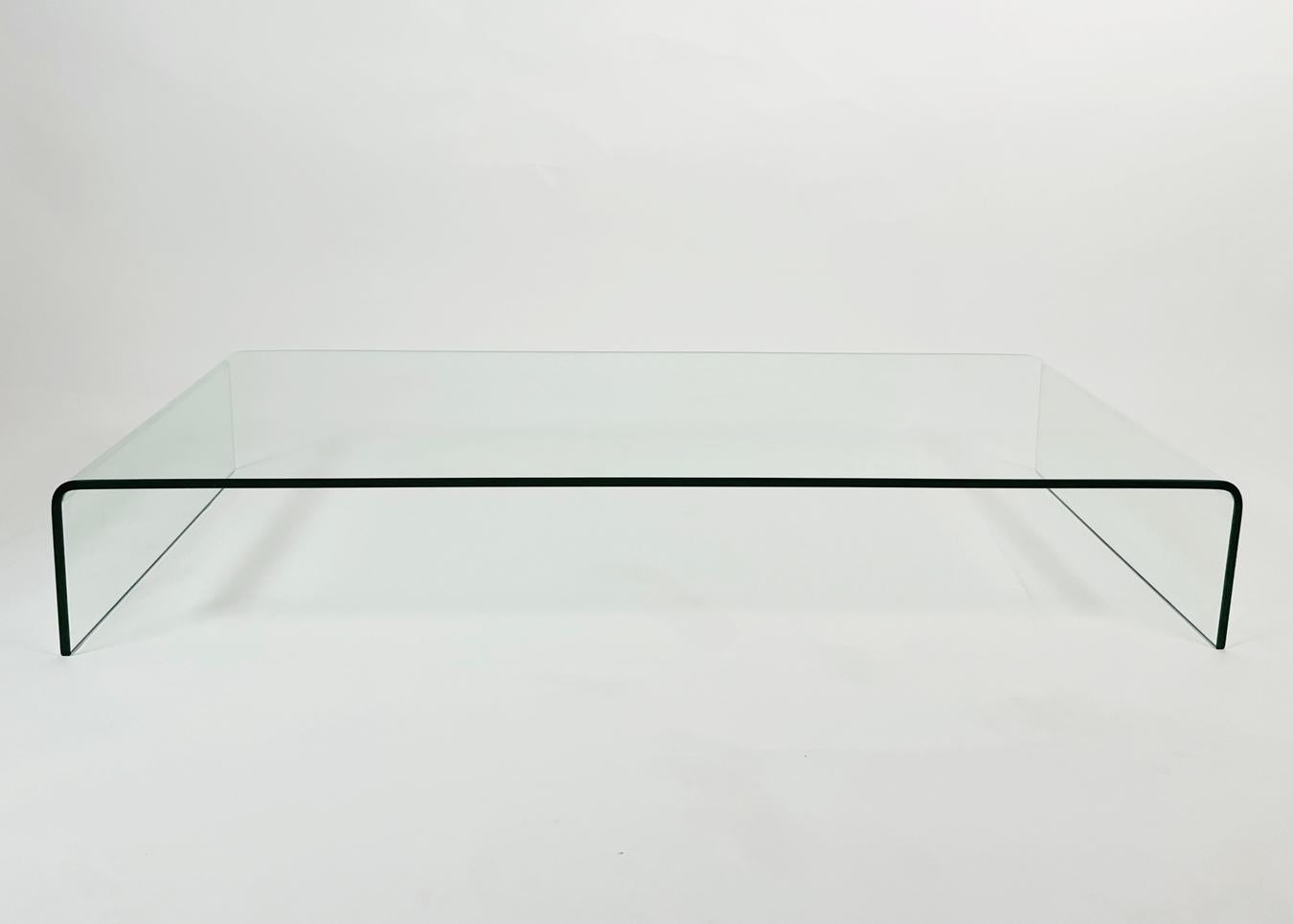 Introducing our stunning Waterfall Coffee Table in Solid Glass. This exquisite piece of furniture is crafted from high-quality glass, providing a sleek and modern look to any living room. The table features curved edges that create a cascading