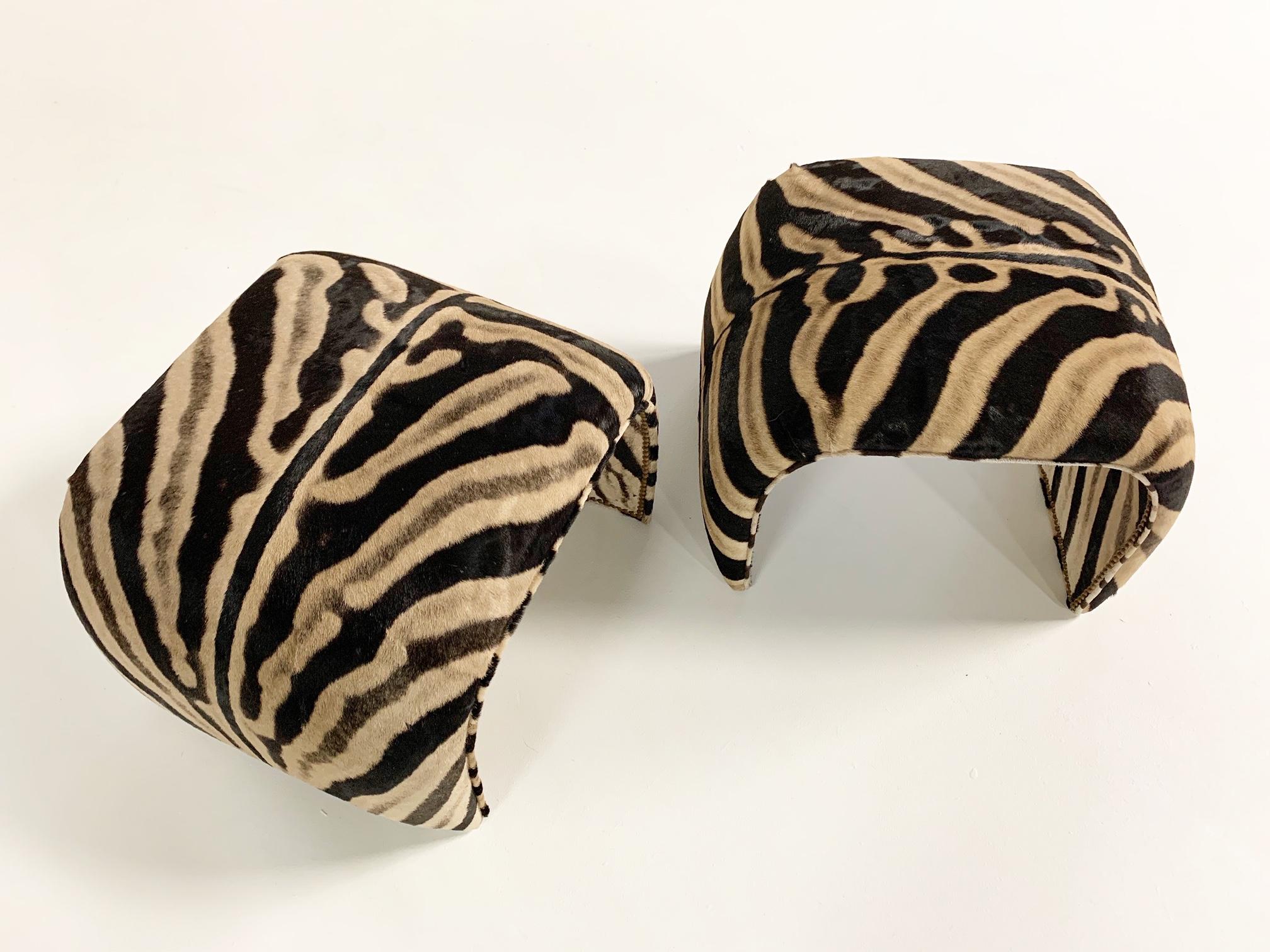 We collected these ottomans for their unique shape. The entire piece has been meticulously reupholstered in zebra hide. There is no seam on the top and brass nailheads finish the seam on the underside. They are beautiful and would look lovely in