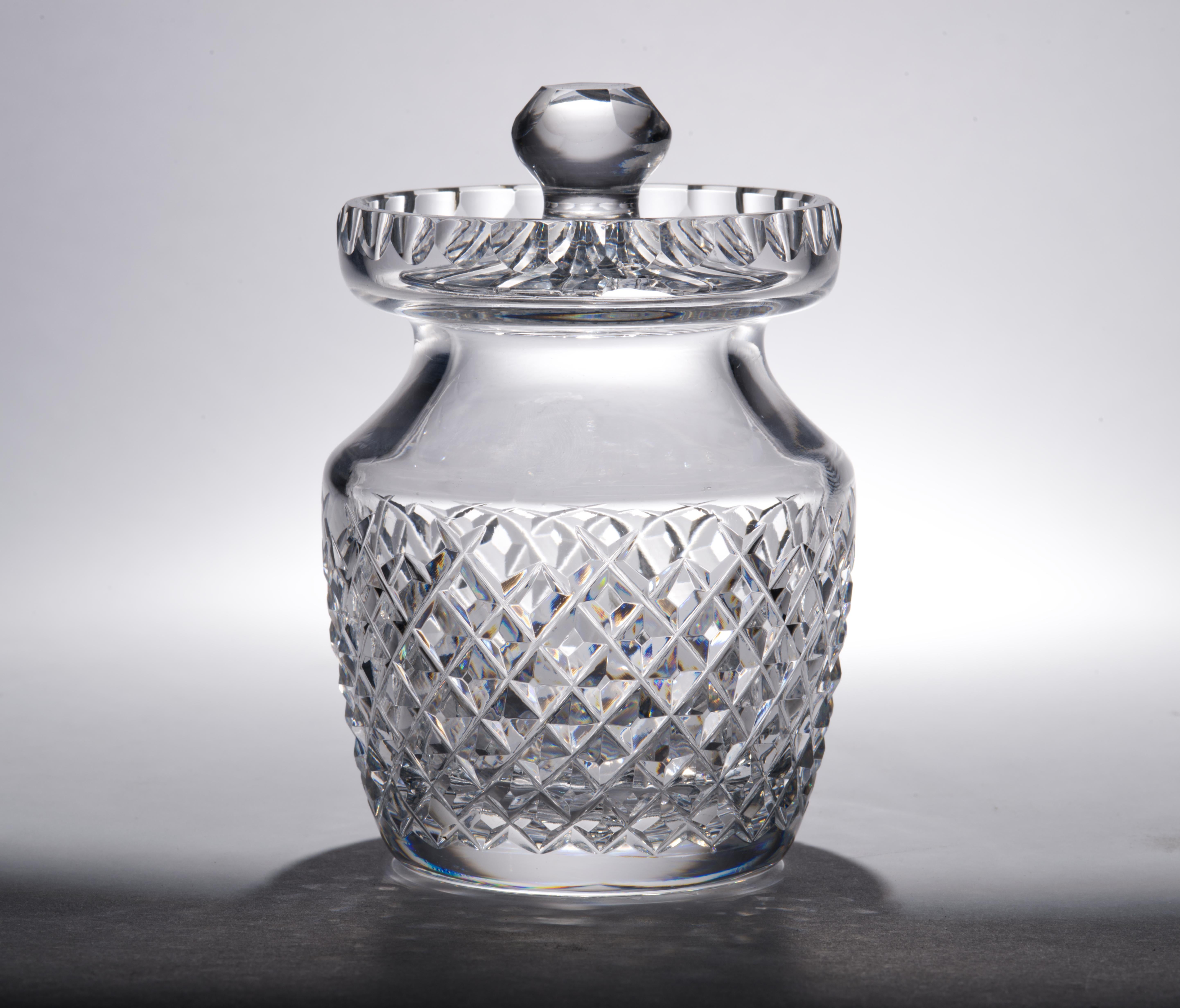  Ce pot de miel en cristal taillé vintage avec couvercle a été fabriqué par Waterford dans le motif Alana. Le motif a été fabriqué de 1952 à 2022 ; il se caractérise par des hachures transversales. Le pot lourd et stable est surmonté d'un bord