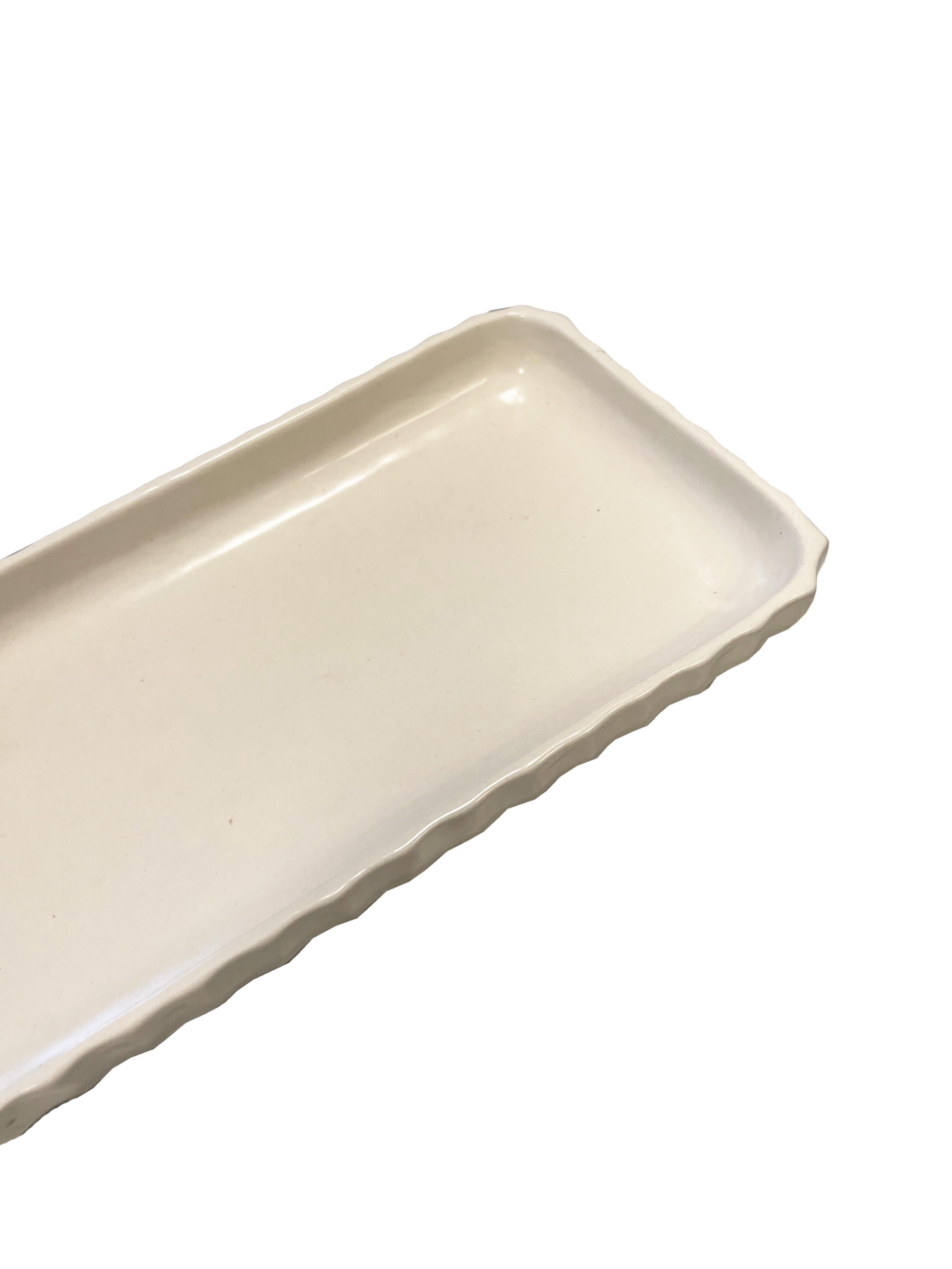 Indulge in the simple elegance of this ivory white ceramic tray, thoughtfully designed by Waterworks. This exquisite piece stands out with its charming scalloped edge detail, a design choice that infuses a touch of whimsy and refined grace into any