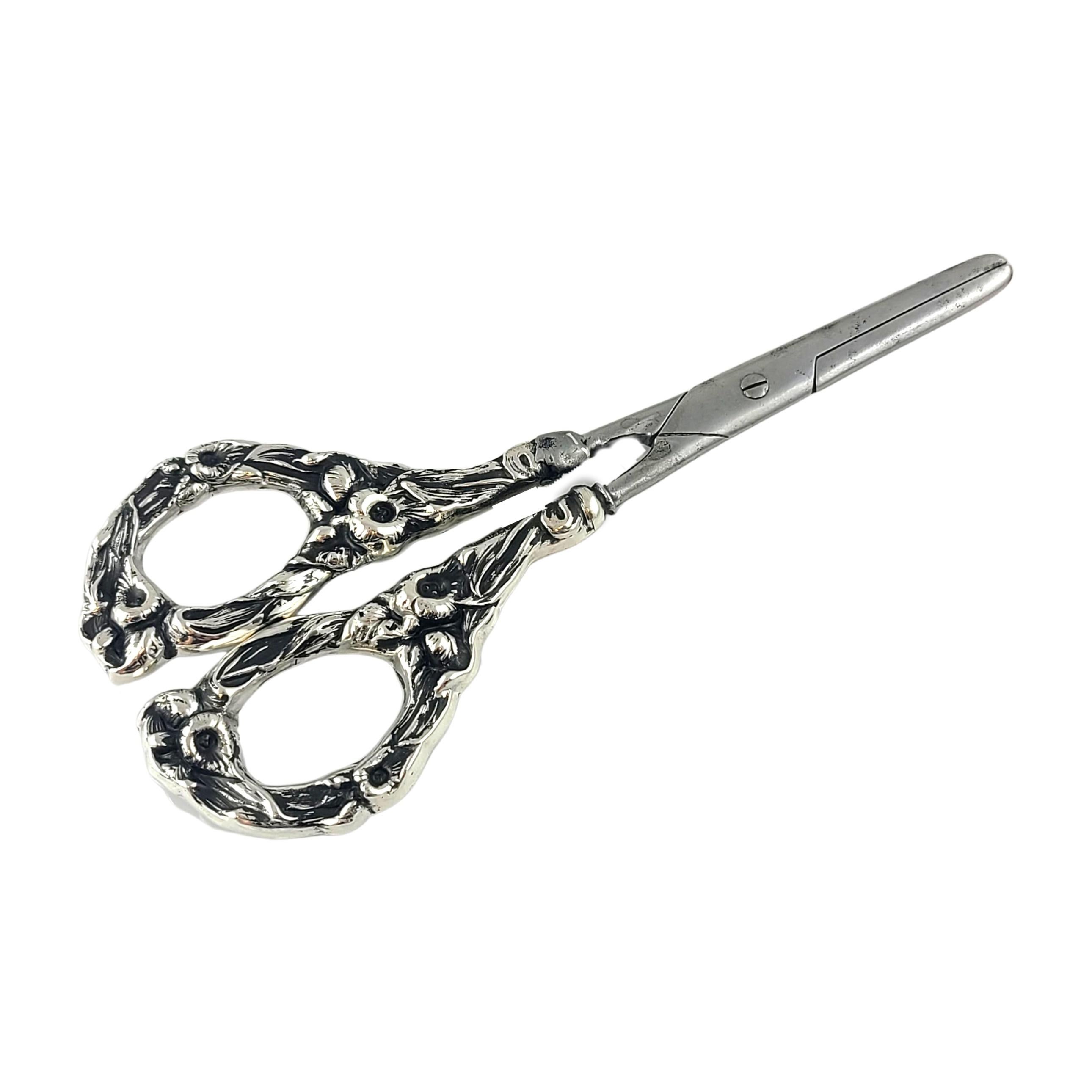 Sterling silver grape shears/scissors by Watson.

Monograms appear to be THJ and 1900.

Watson of Attleboro, MA were manufacturers of silver novelties from 1880-1950. These grape shears feature floral sterling handles and German stainless steel
