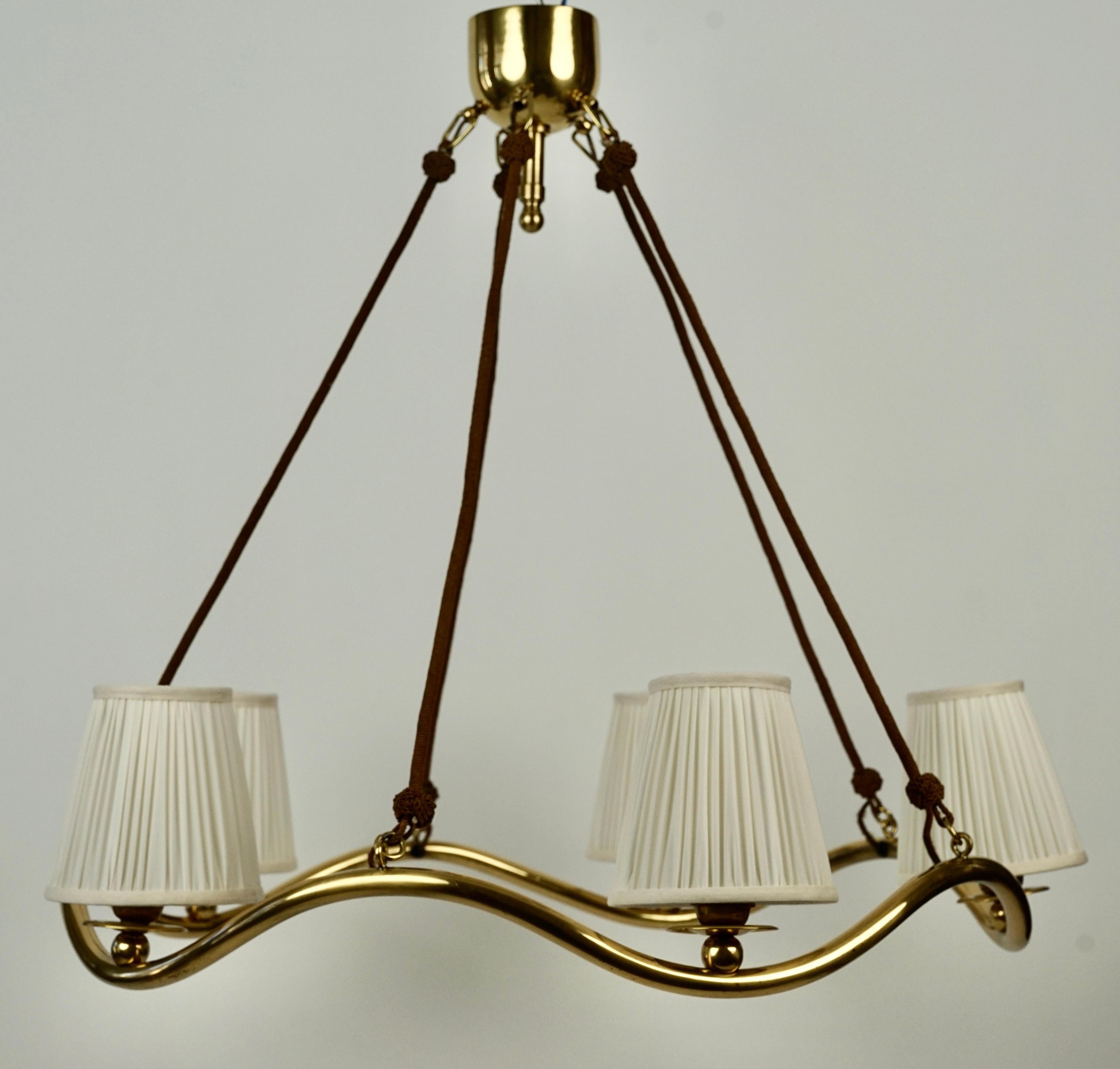  Lustre Wave conçu par Oswald Haerdtl vers 1934, en laiton poli avec cinq abat-jours en soie.
Les luminaires de cette version s'inclinent légèrement vers l'intérieur, de la soie a été utilisée pour récupérer les cadres. Le laiton
Le métal a été