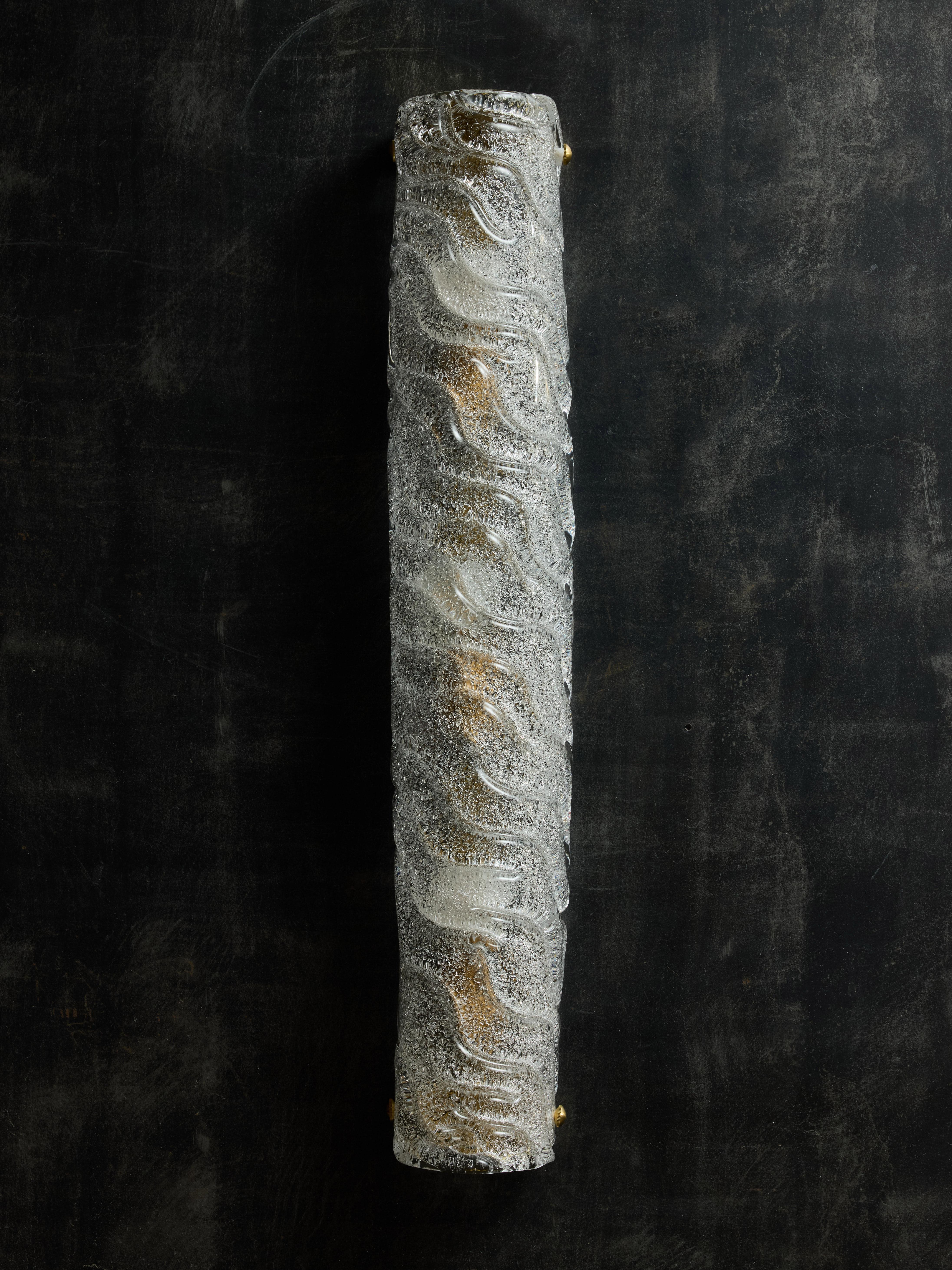 Applique tubolari realizzate con un pezzo di vetro di Murano con motivi a onde e una texture ruvida all'interno che rende il vetro chiaro non trasparente e diffonde la luce delle tre lampadine all'interno. La parte superiore e inferiore sono