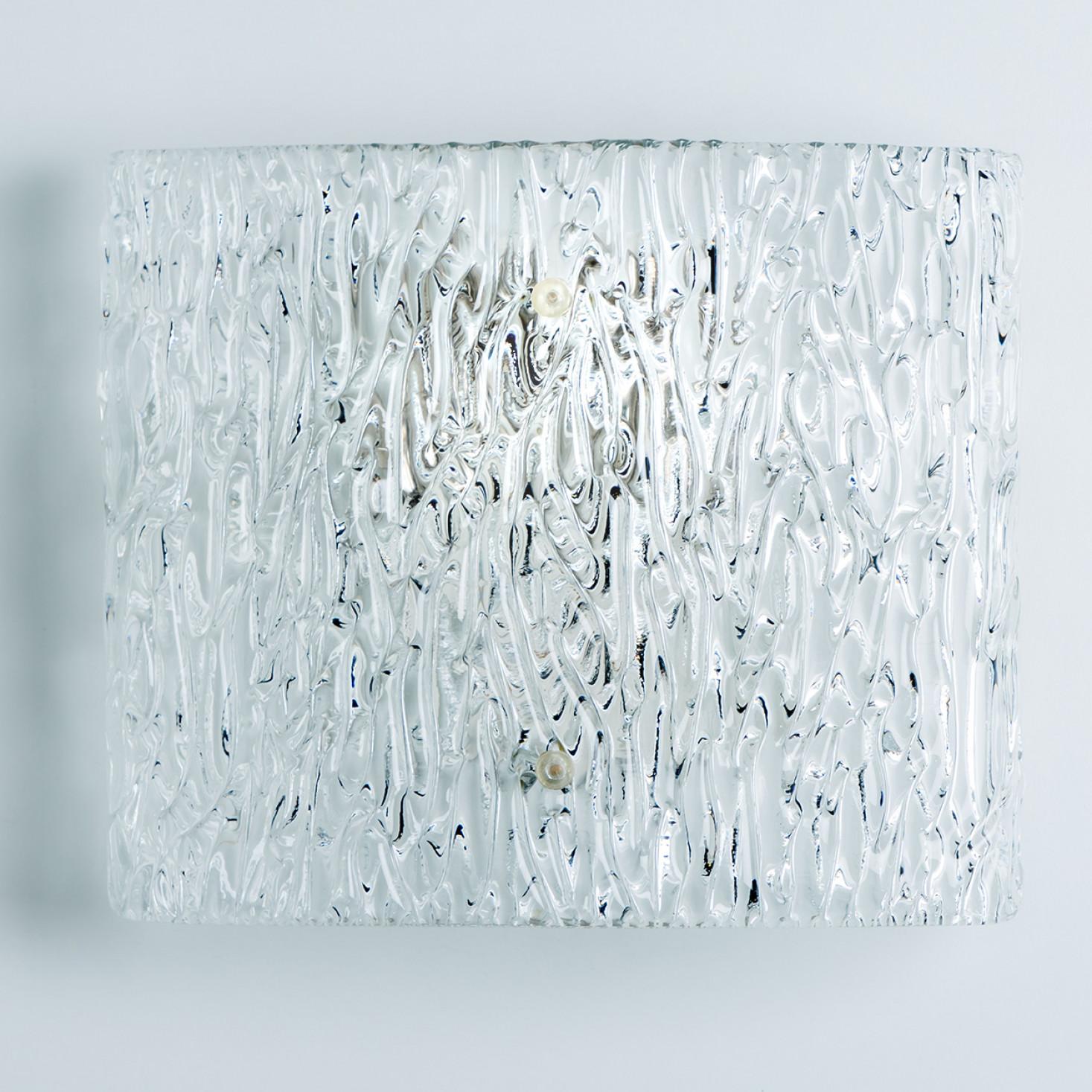 Beautiful high quality light fixture made by Kalmar, Austria. Manufactured in mid century, circa 1970 (at the end of 1960s and beginning of 1970s).

This wall light features lights made of handmade wave ice glass and silver back plate. The sides