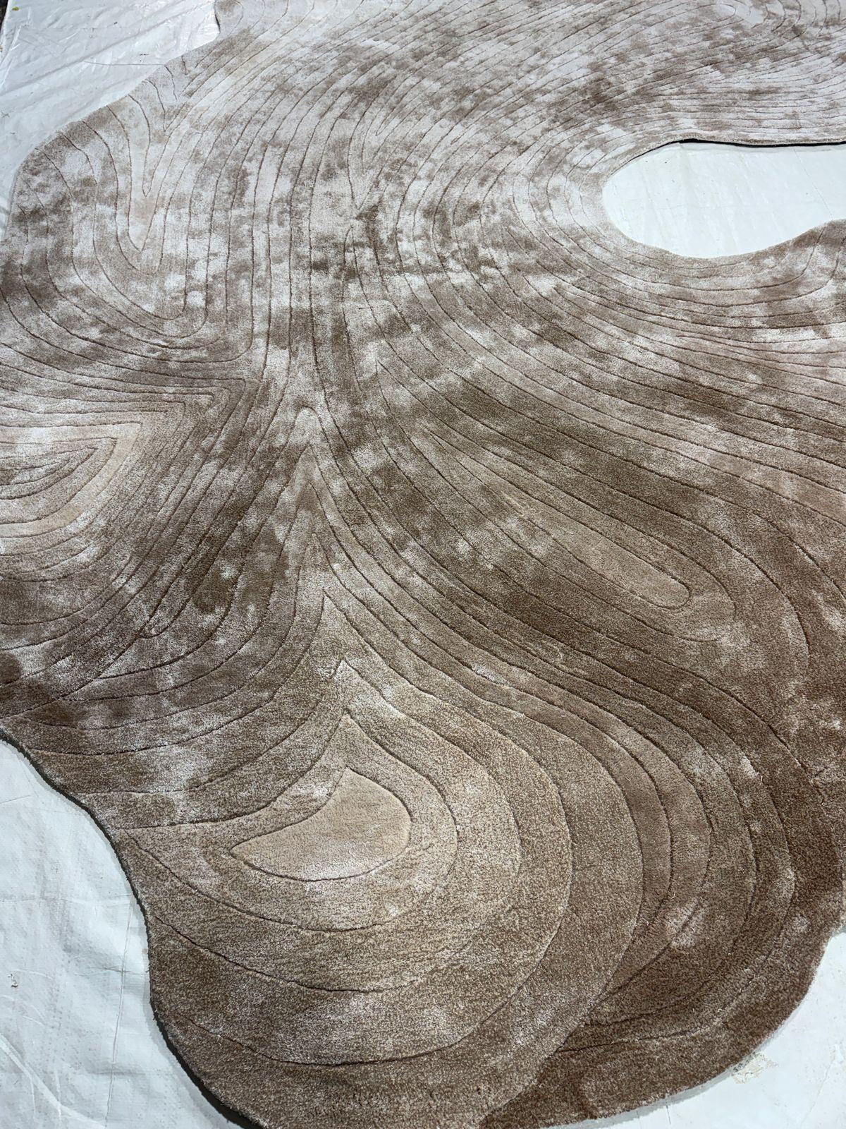 ONDAS es una alfombra orgánica de forma libre inspirada en el movimiento cambiante del agua y el viento. Las fluidas líneas de contorno ondulan por la superficie en capas de tonos topo y arena, creando una meditativa sensación de movimiento y