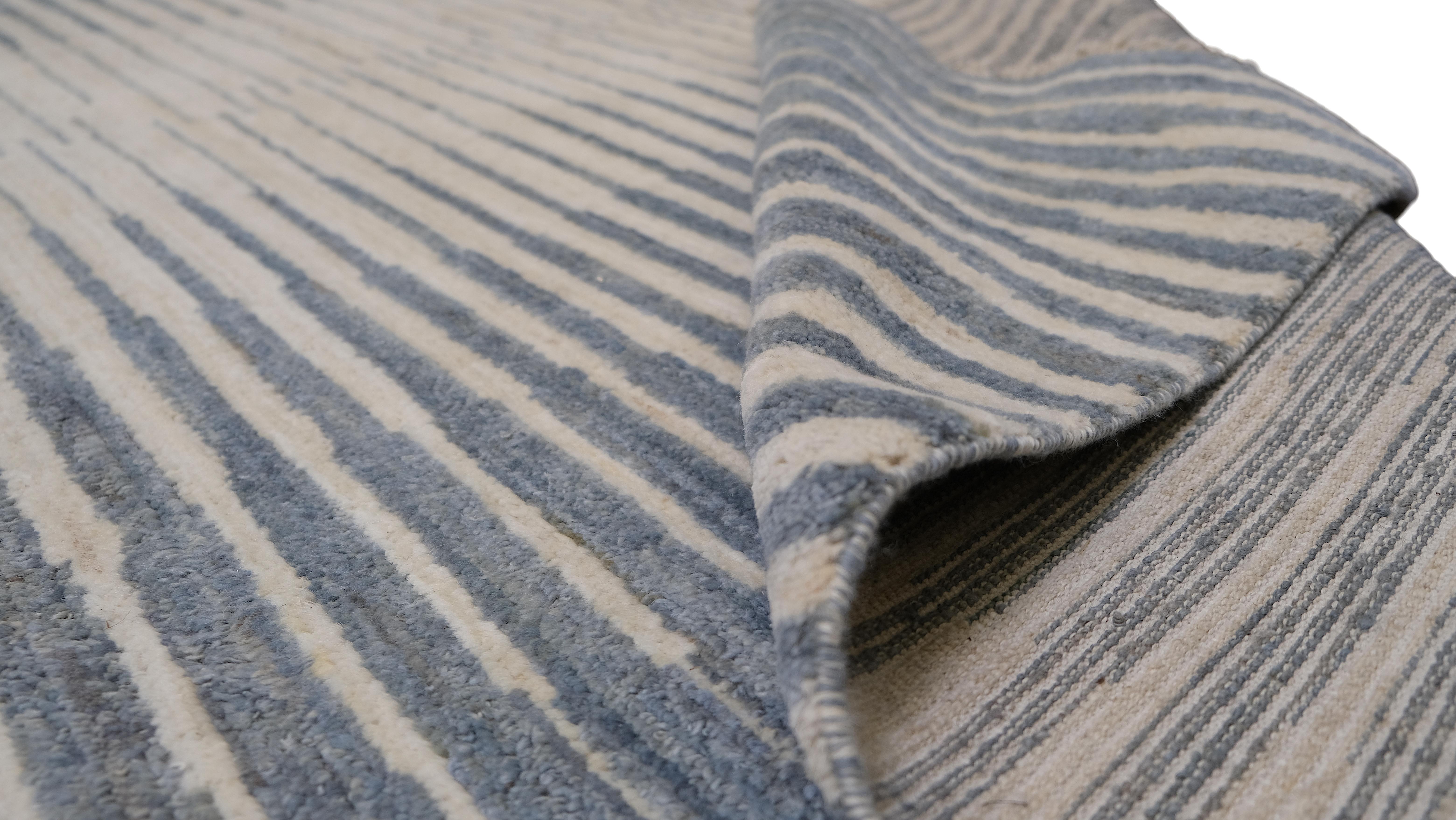 Dona un tocco di contemporaneità ai tuoi interni con questo raffinato tappeto in lana annodato a mano. Caratterizzato da un accattivante motivo a strisce in un gradiente di tonalità blu e avorio, questo tappeto emana raffinatezza ed eleganza. Il suo