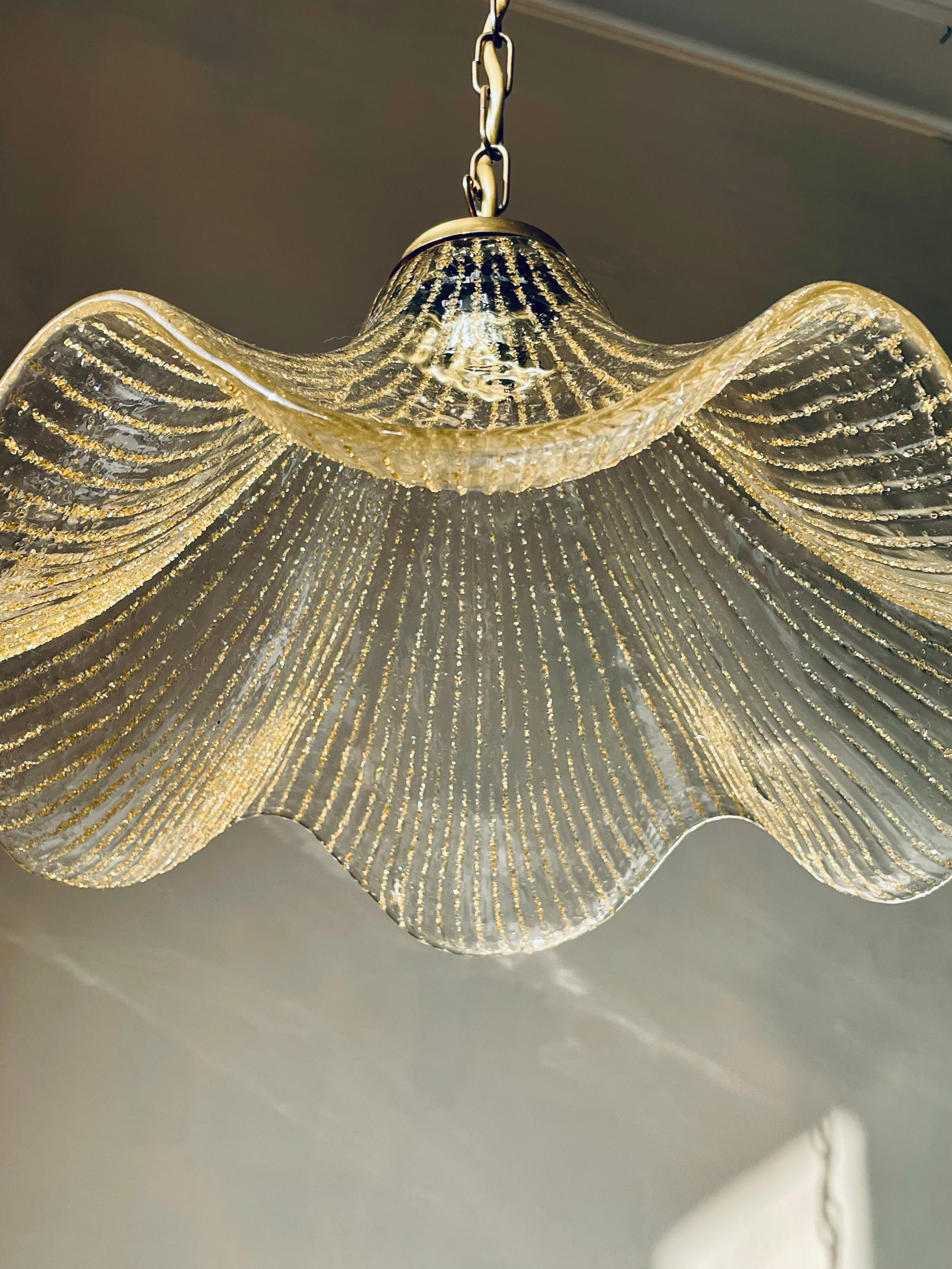 Stunning vintage Murano art glass pendant with a wide, wavy appearance resembling a large golden flower. The clear thick mouthblown glass is soft and smooth on the outside while thousands of small golden accents create bright lines on the inside